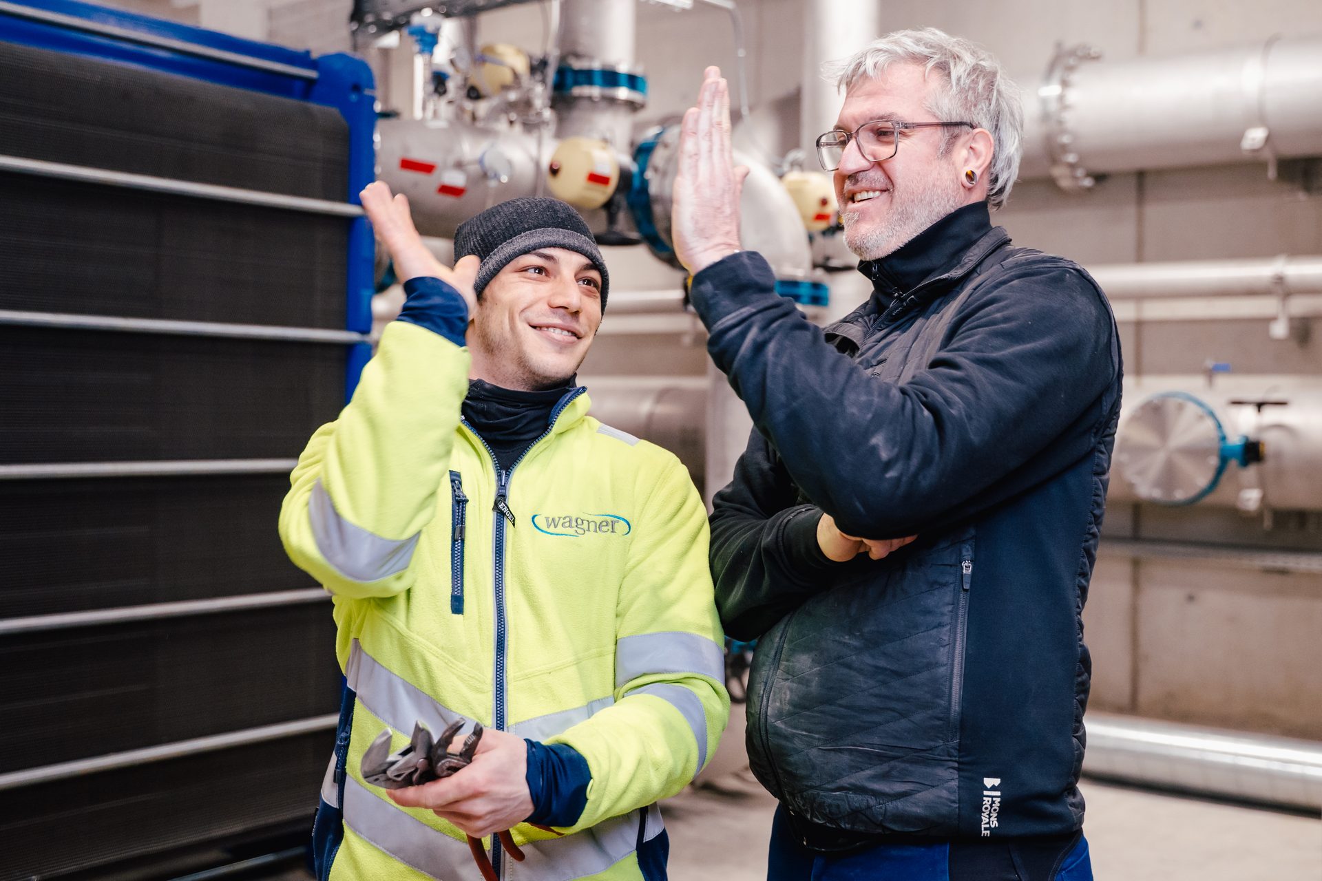 Two smiling workers high-fiving in an industrial setting, symbolizing teamwork and success.