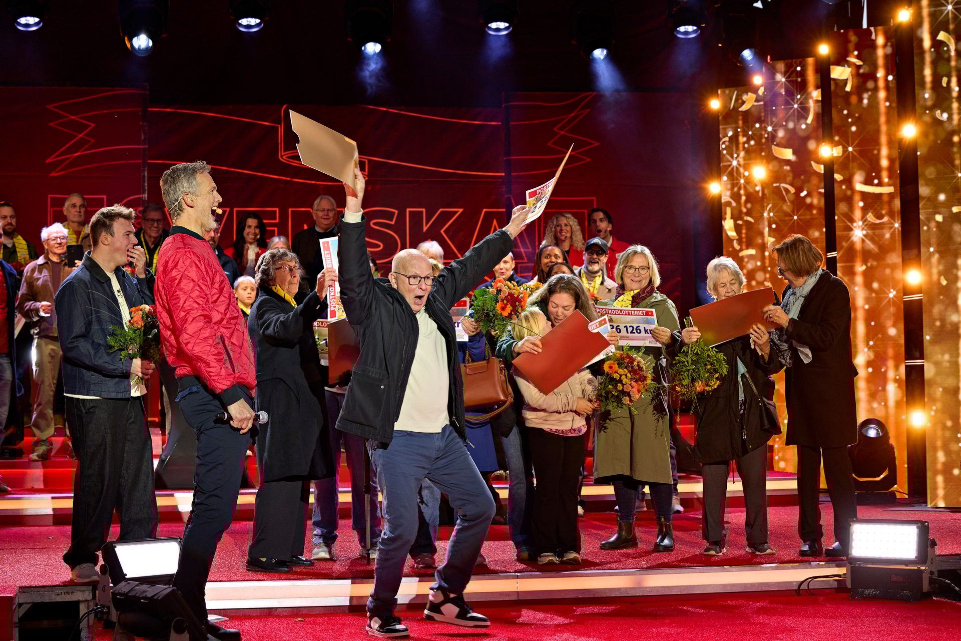 Joyful group on a red stage celebrating winnings with large checks, one man cheering enthusiastically.