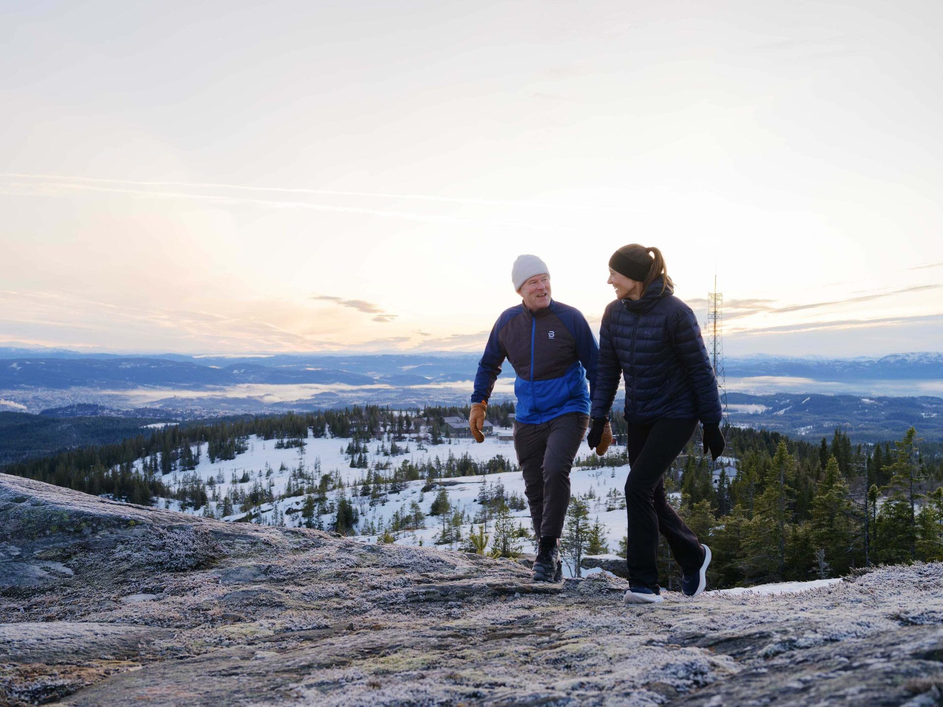 Two hikers on a snowy trail overlooking a winter landscape.