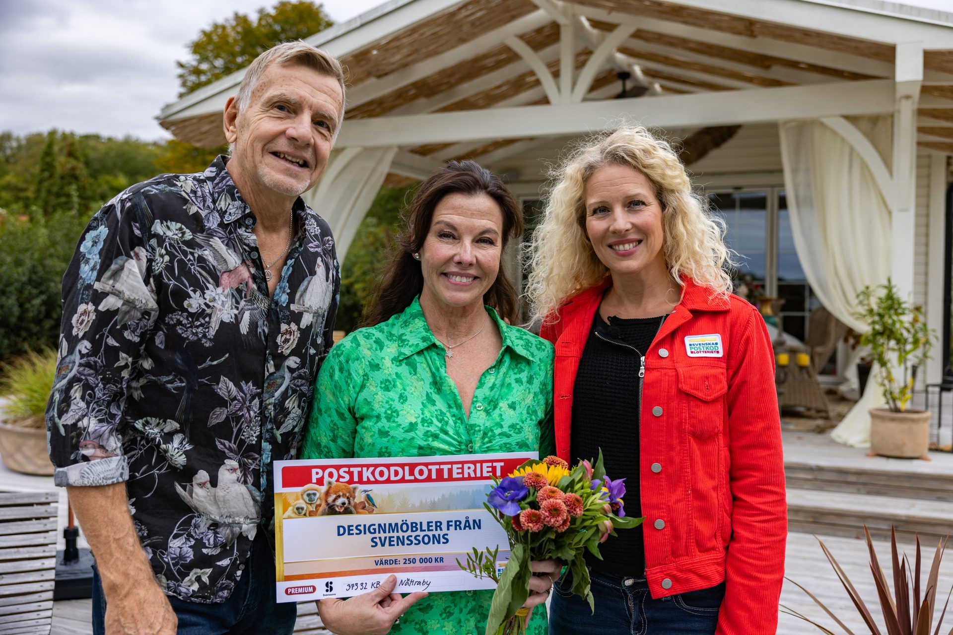 Three smiling people holding a large Postkodlotteriet prize check for 250,000 KR design furniture.