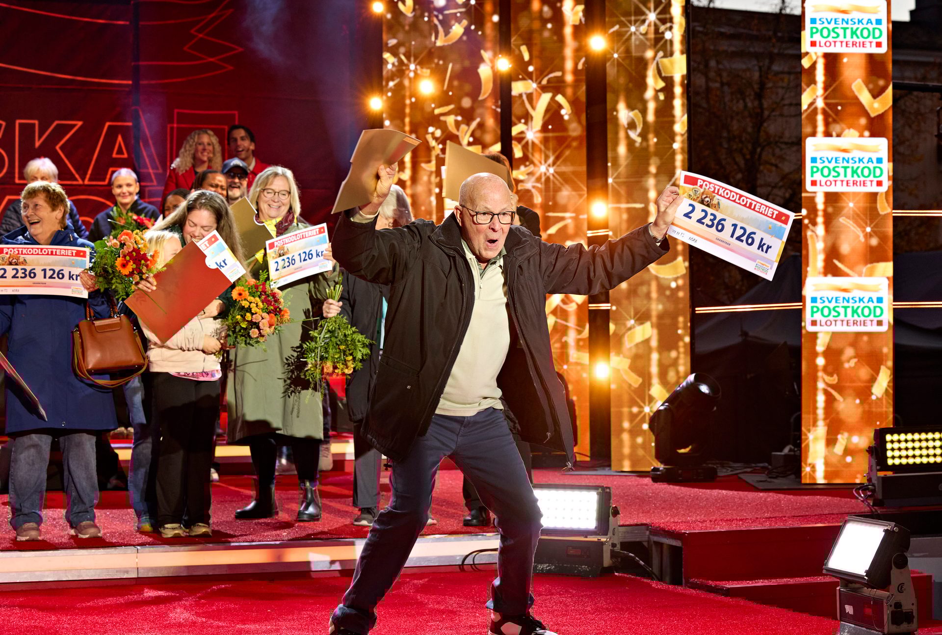 Exuberant man and lottery winners on stage with checks for 2,236,126 kr.