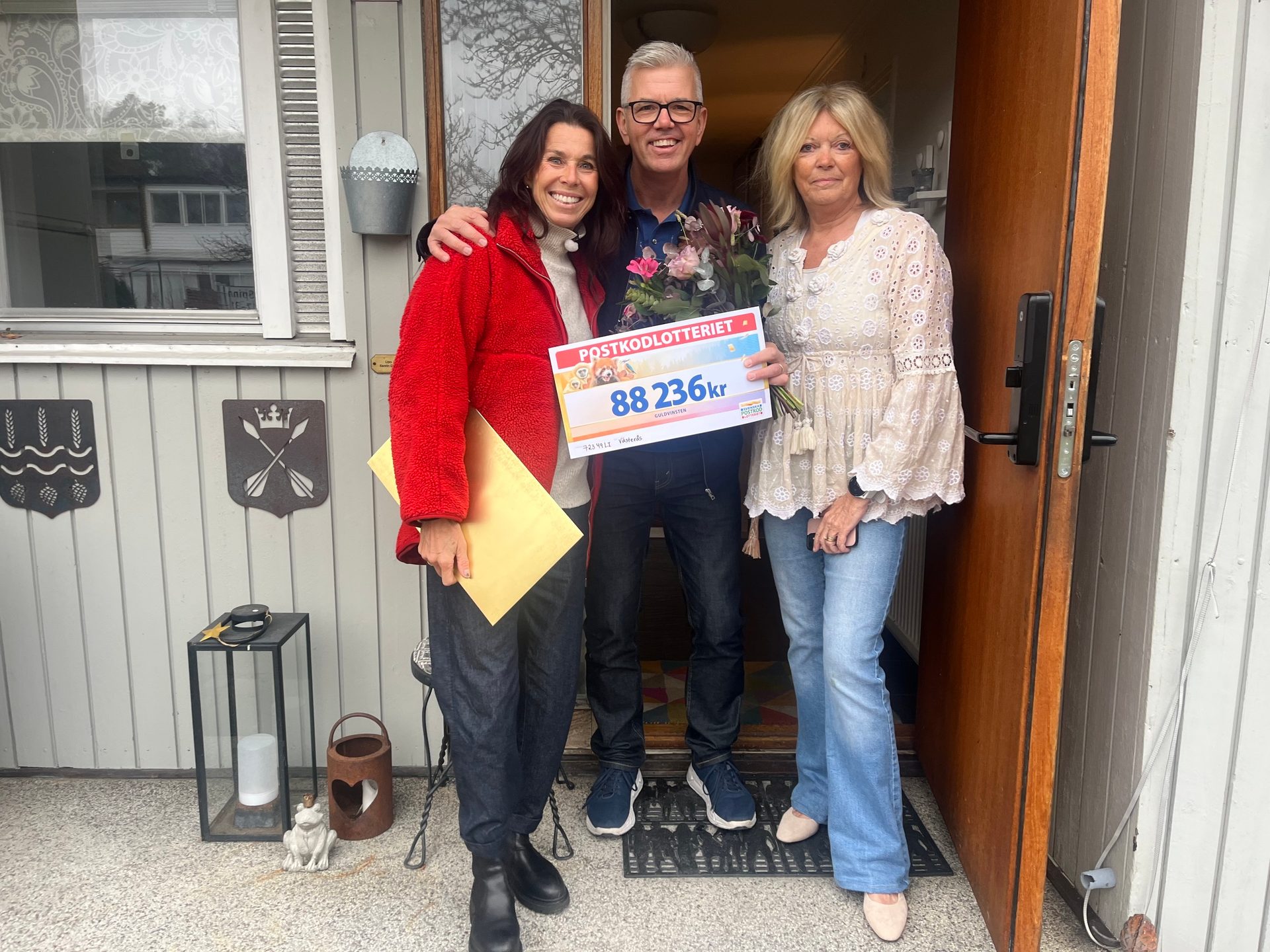 Three smiling people pose with a large check from "Postkodlotteriet" for 88,236 kr.