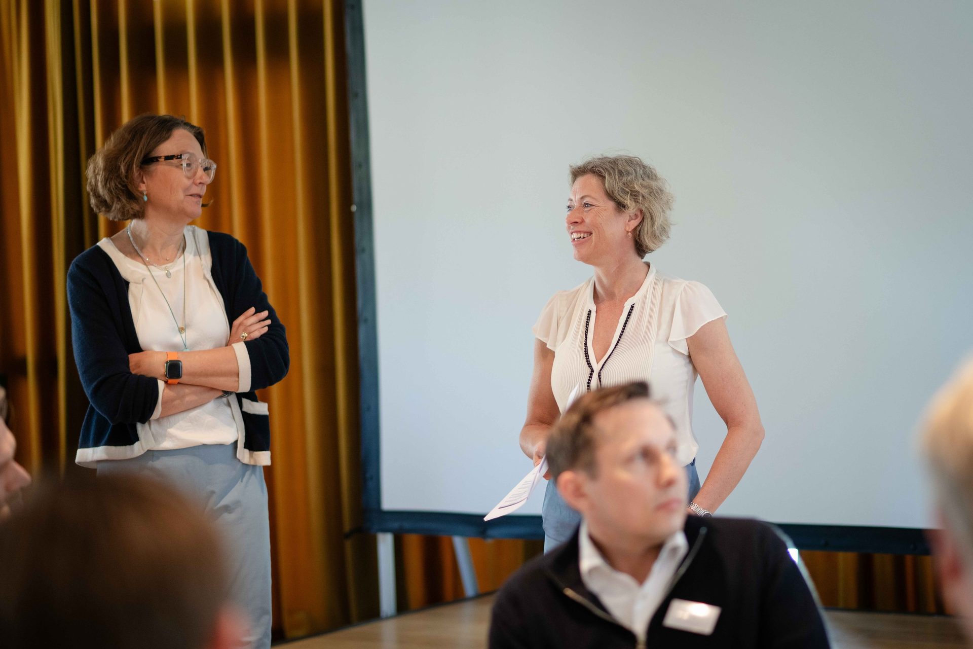 Two women interact in a meeting; one smiles and speaks, the other listens.
