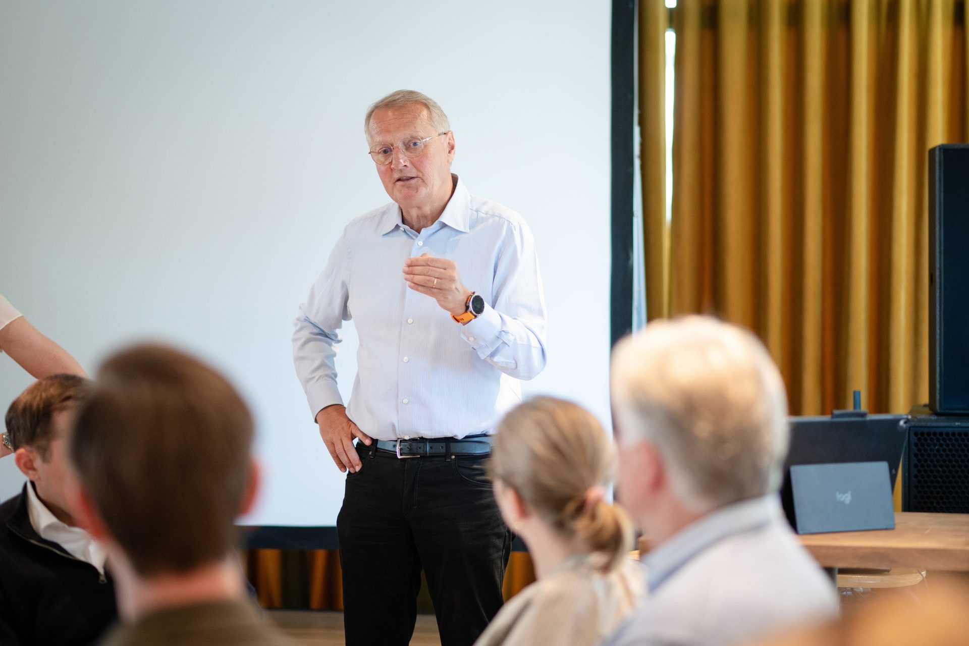 Older man in blue shirt and glasses speaking to an audience.