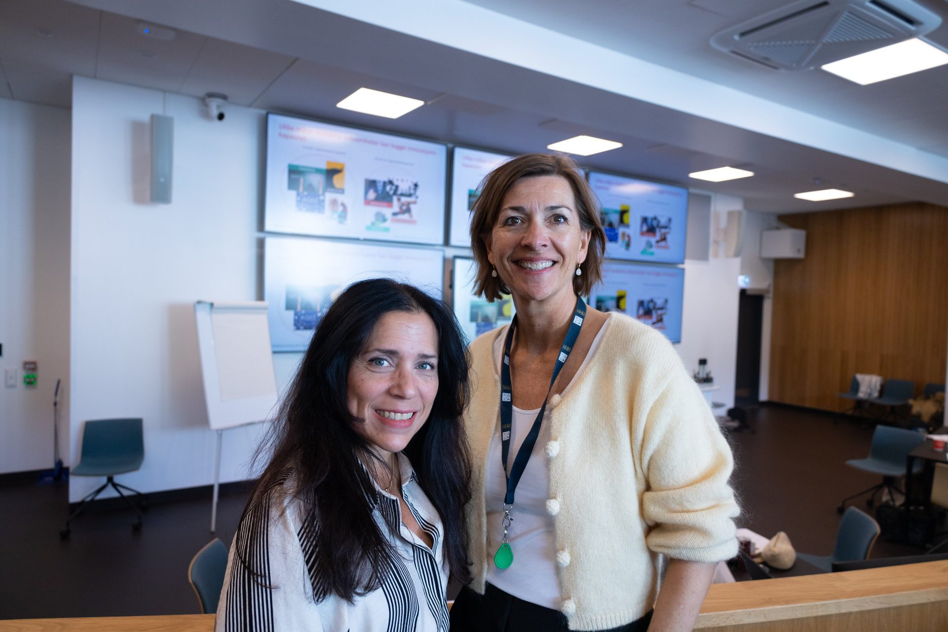 Two smiling women in a modern office with multiple digital screens.