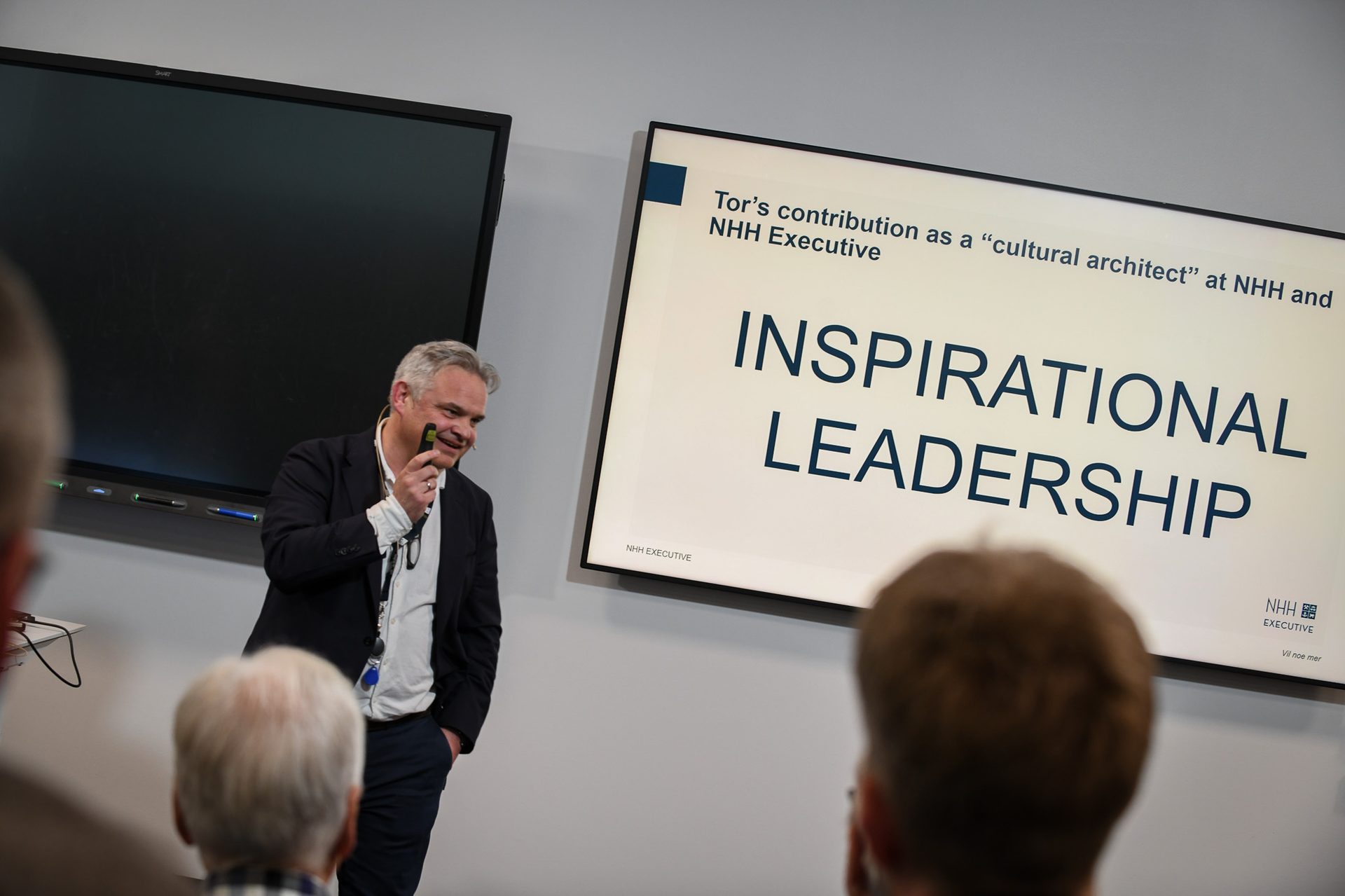 A man speaks beside a screen displaying "INSPIRATIONAL LEADERSHIP" and "Tor's contribution at NHH Executive".