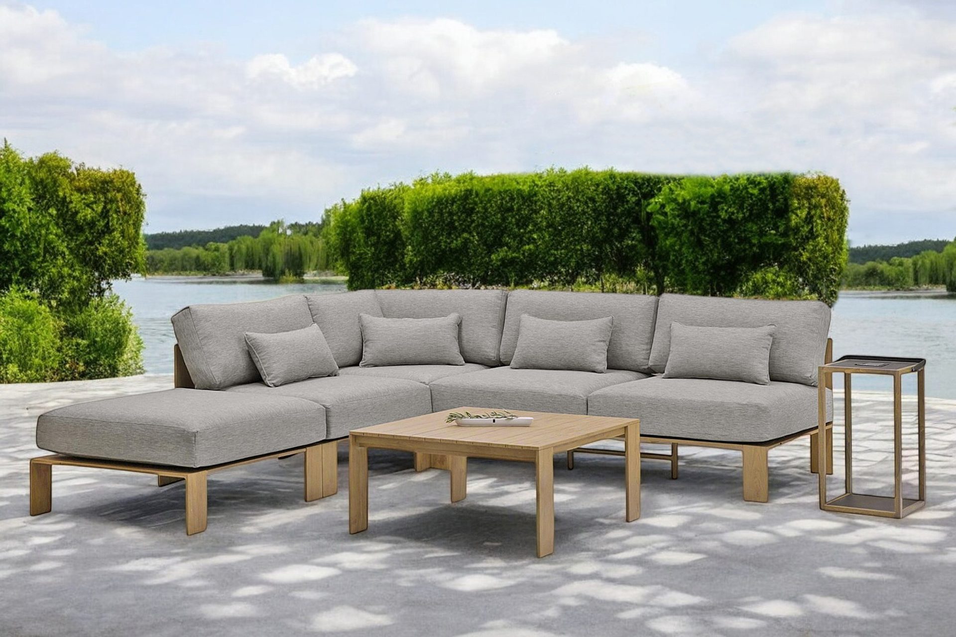 Modern outdoor grey sectional sofa set on a patio by a lake with lush greenery.
