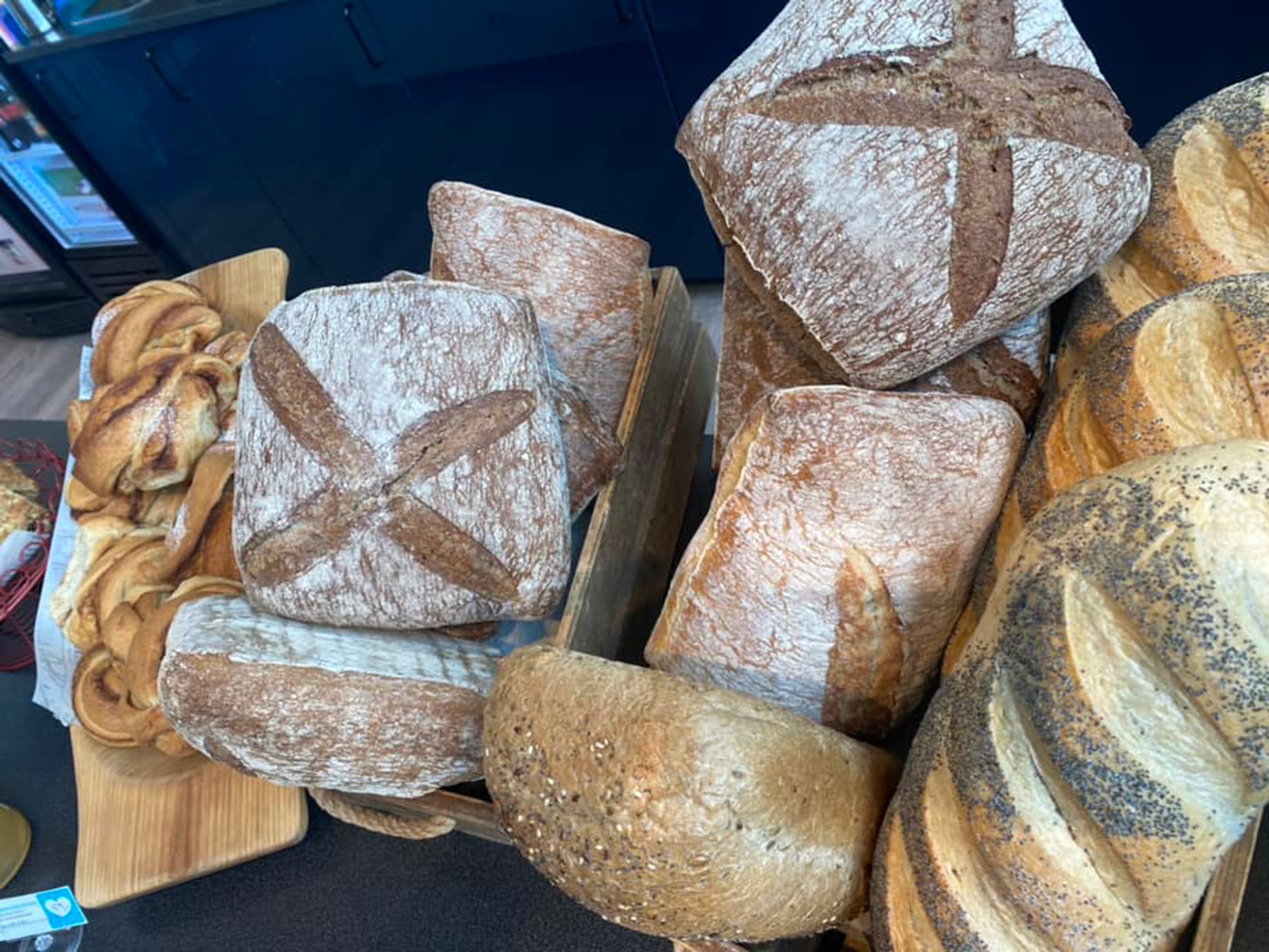 A rustic display of various fresh artisan bread loaves, including sourdough, seeded, and cinnamon roll pastries.