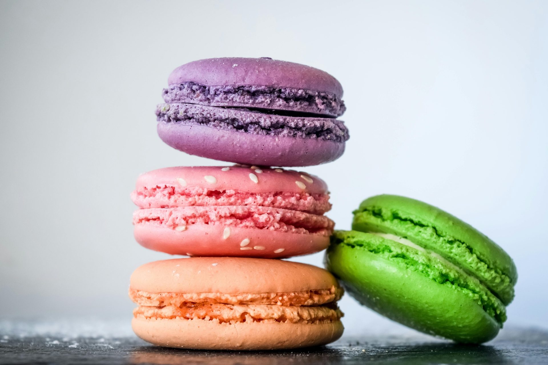 Stack of colorful macarons: purple, pink, orange, plus one green leaning on a dark surface.