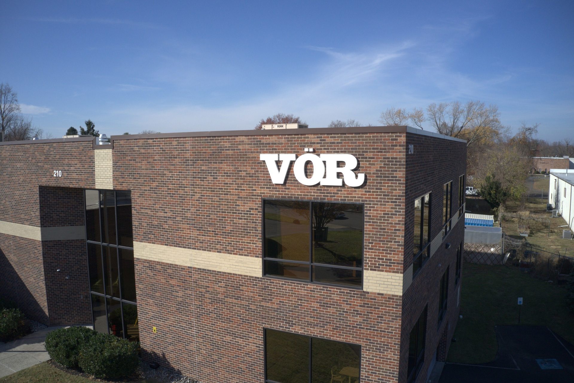 Brick building with "VÖR" sign and "210" on its facade, seen from an aerial perspective.