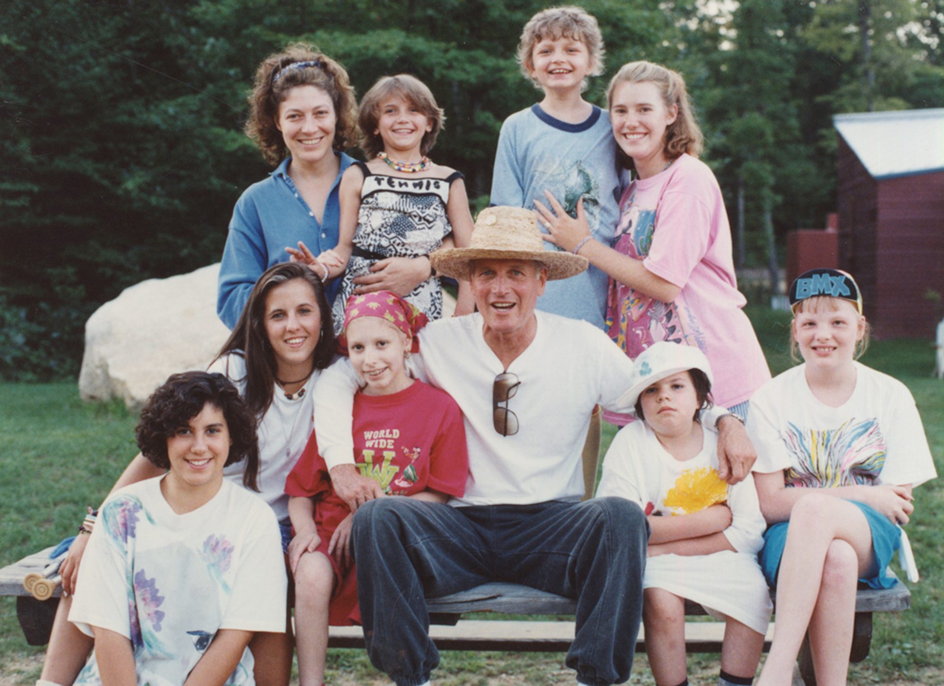 Paul Newman smiles, surrounded by a group of diverse children and young adults outdoors.