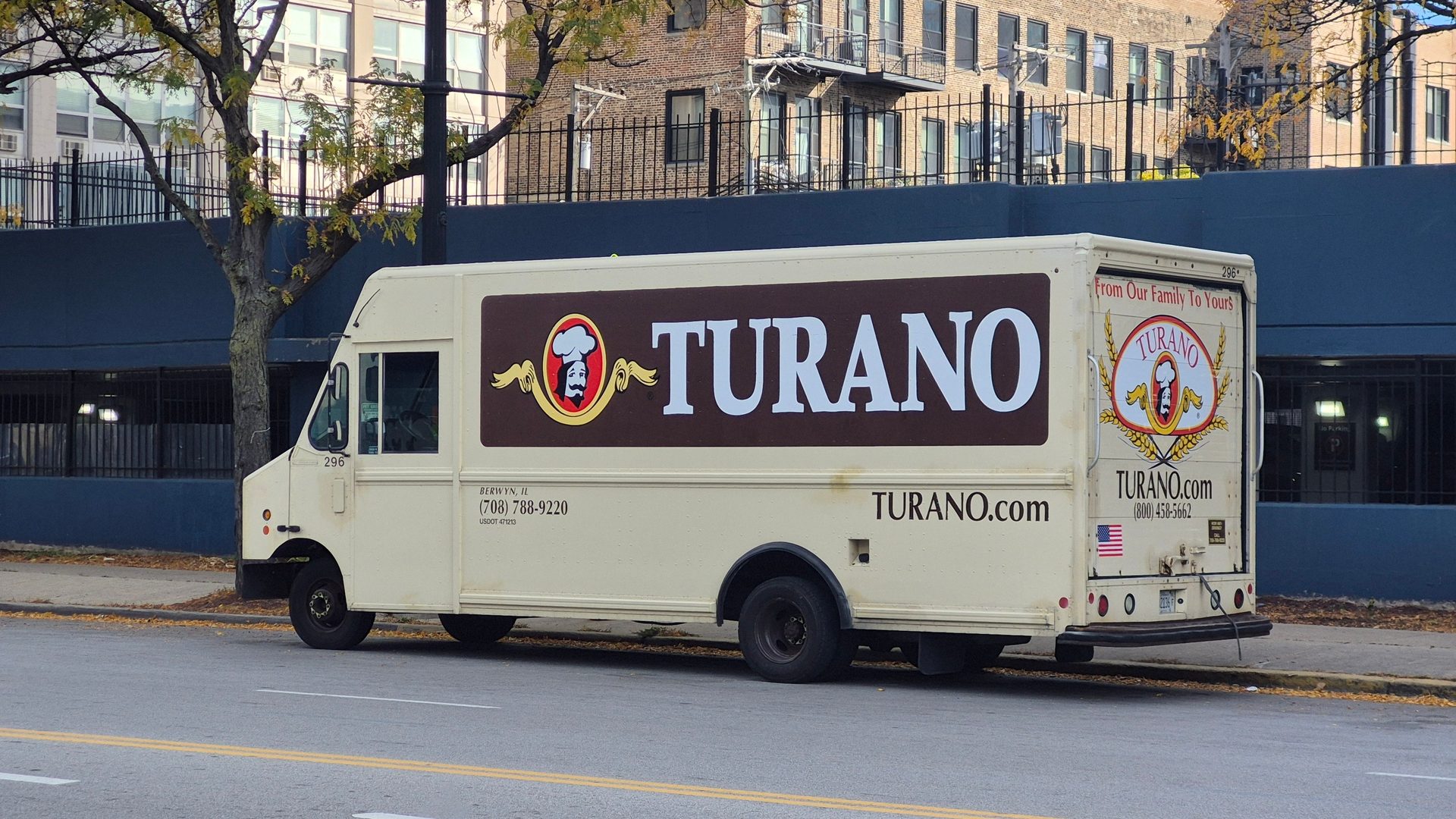 Cream-colored Turano bread delivery truck with a baker logo on its side, parked on a street.