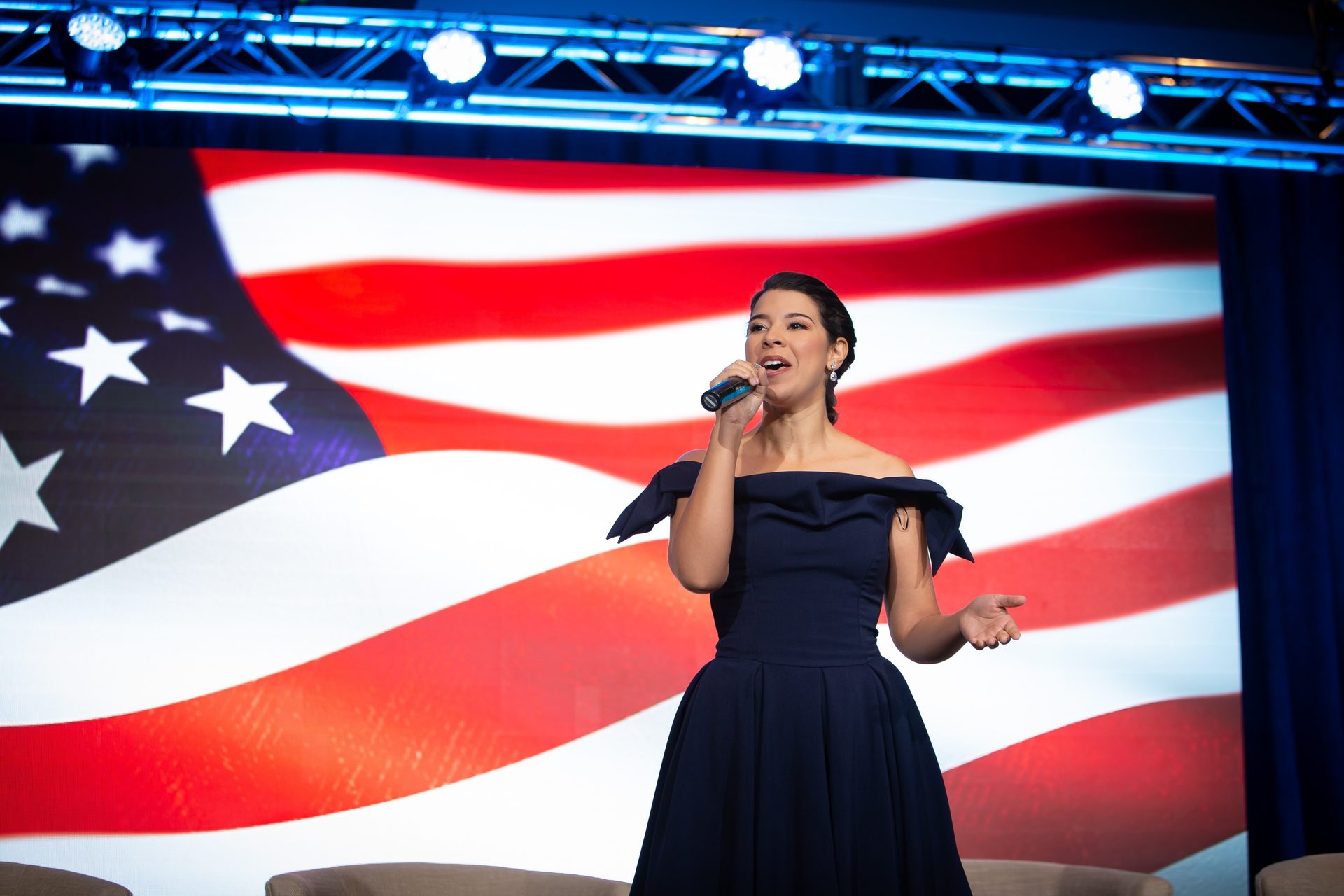 Flag of the united states, Public address system, Performing arts, One-piece garment, Microphone, Dress, Gesture, Entertainment, Red