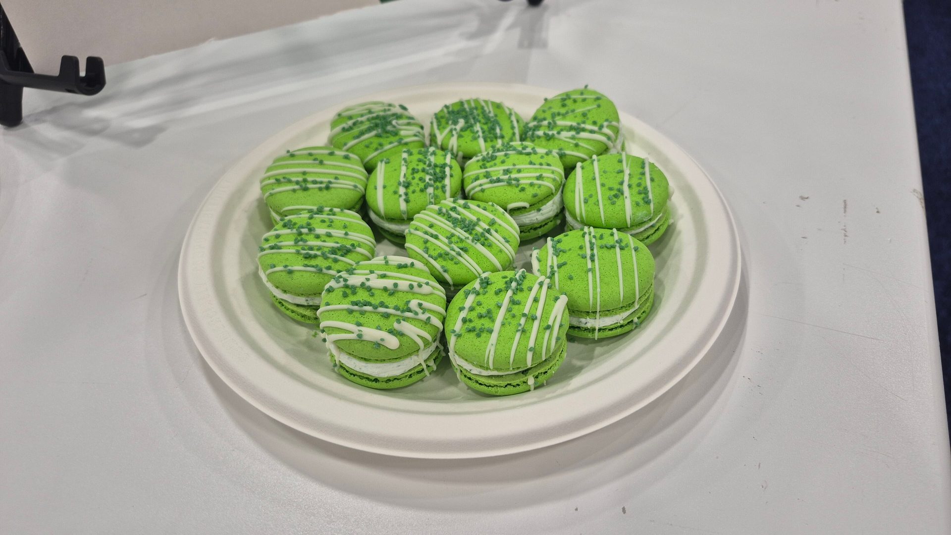 Green macarons with white drizzle and green sprinkles on a white plate.