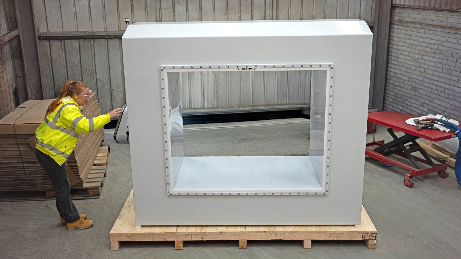 Woman in safety gear operates a large white cleanroom enclosure with a clear viewing window.