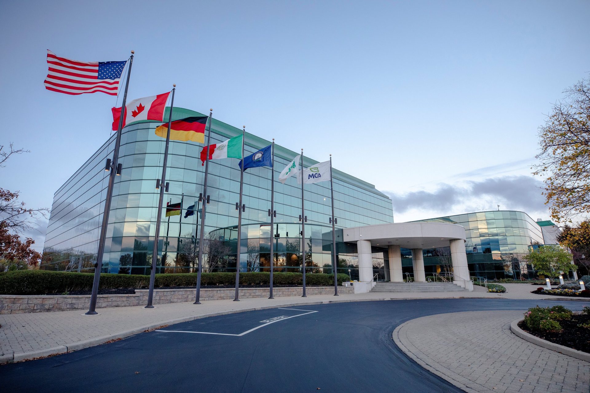 Modern glass building with a row of international and company flags flying in front on a clear day.