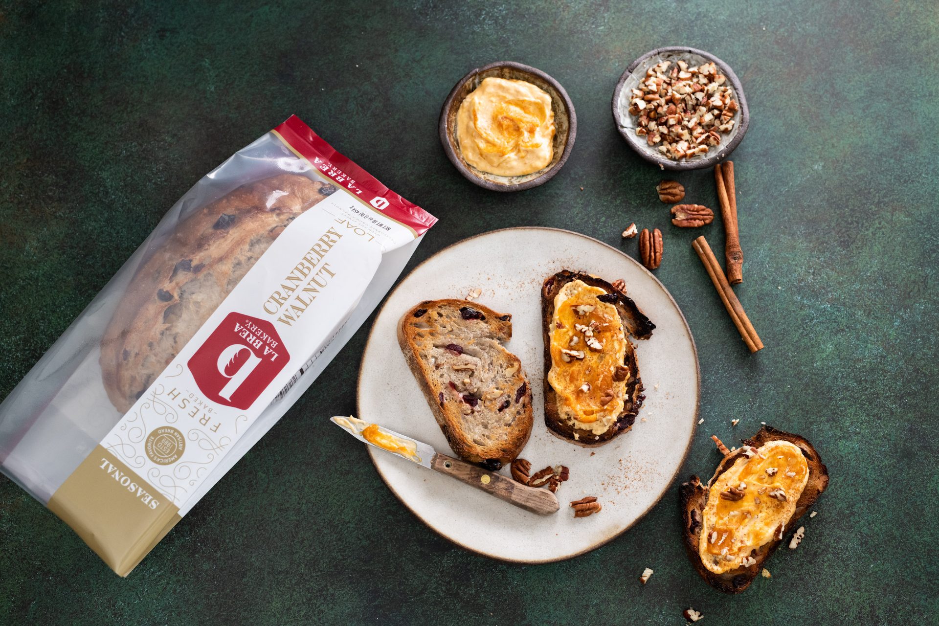 Cranberry Walnut Loaf in packaging, Table, Spread, Knife, Bowls, Cinnamon sticks, Slice