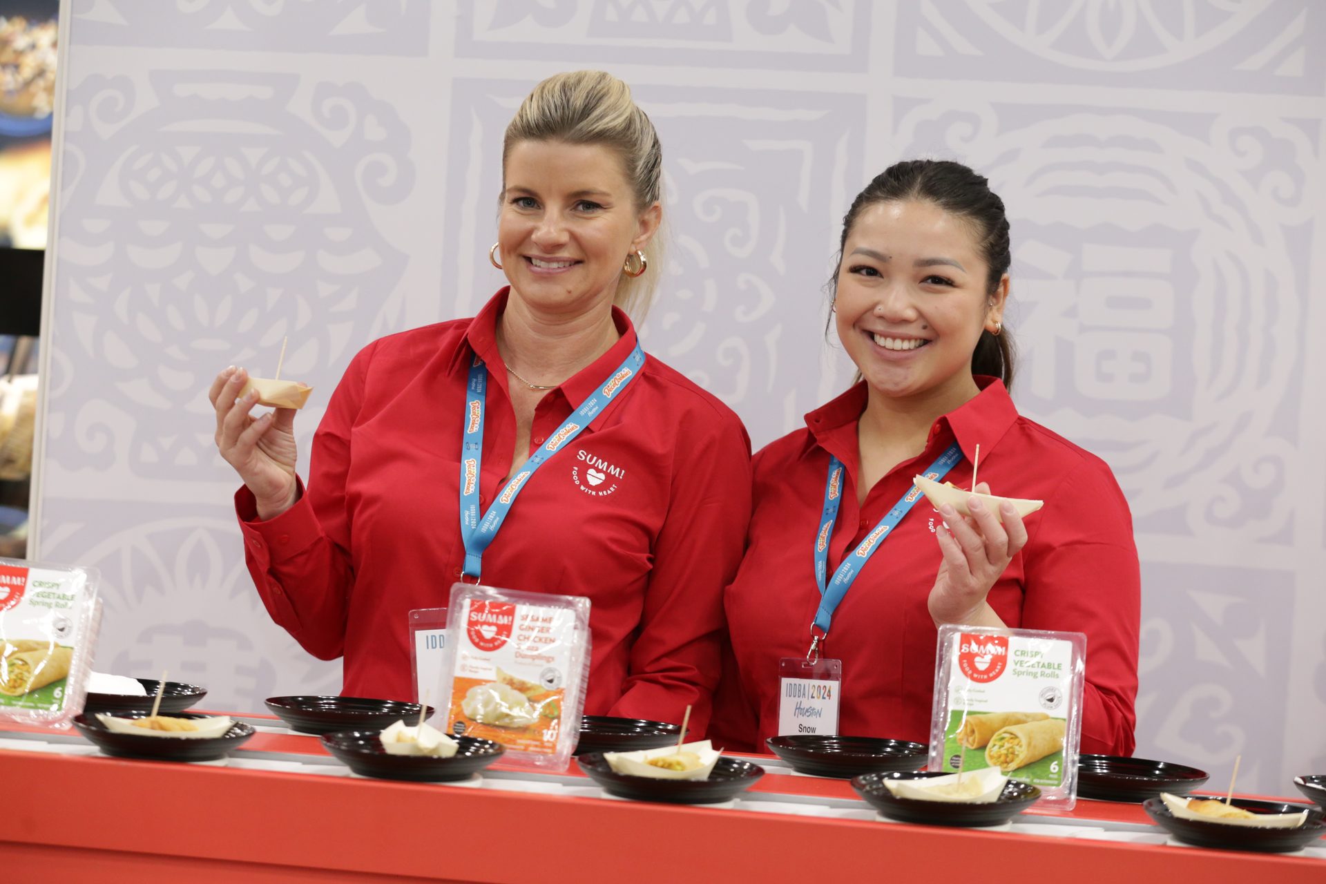 Two women hold up samples of dumplings and spring rolls at IDDBA