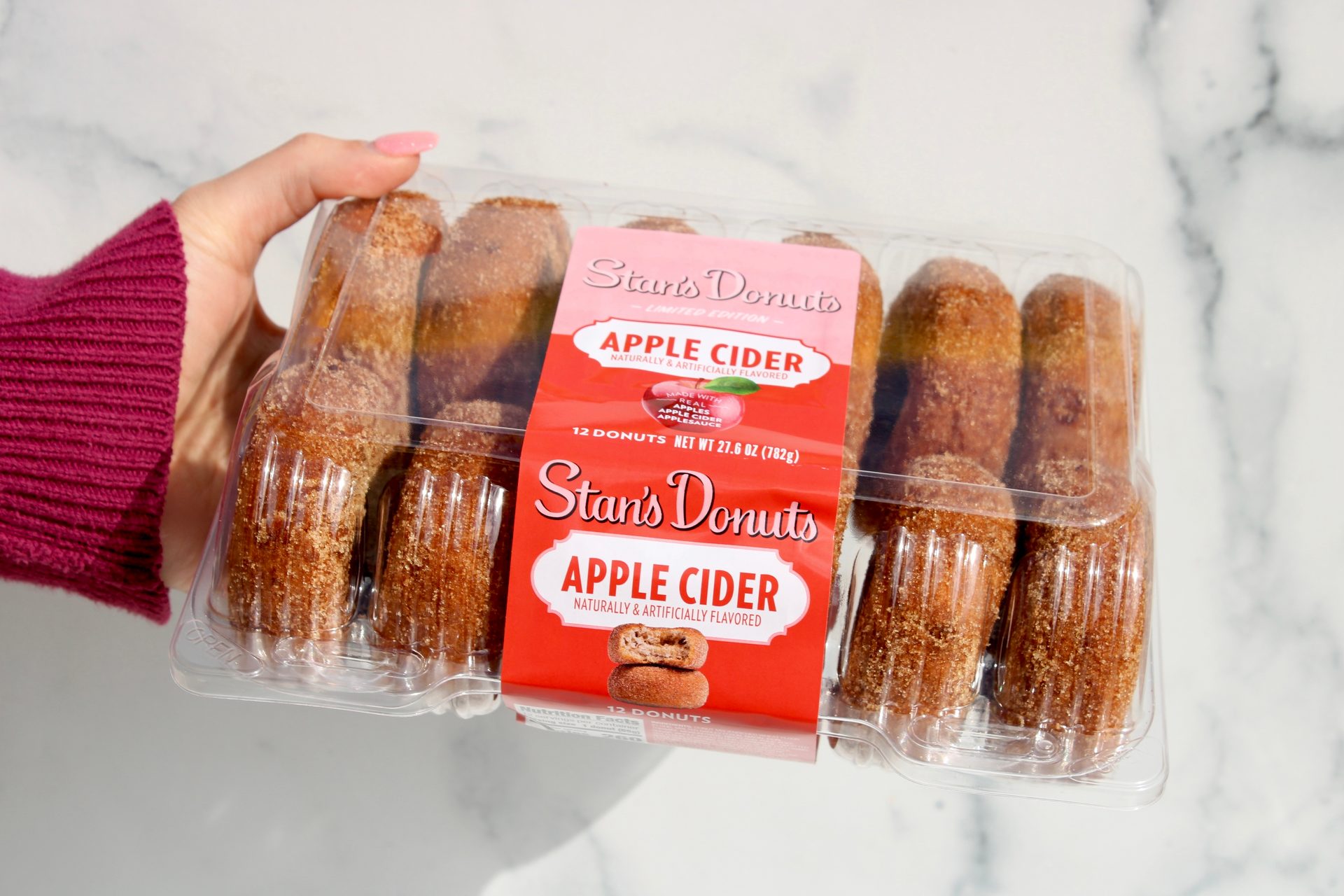 Hand holding a clear container of Stan's Apple Cider Donuts, 12 count.