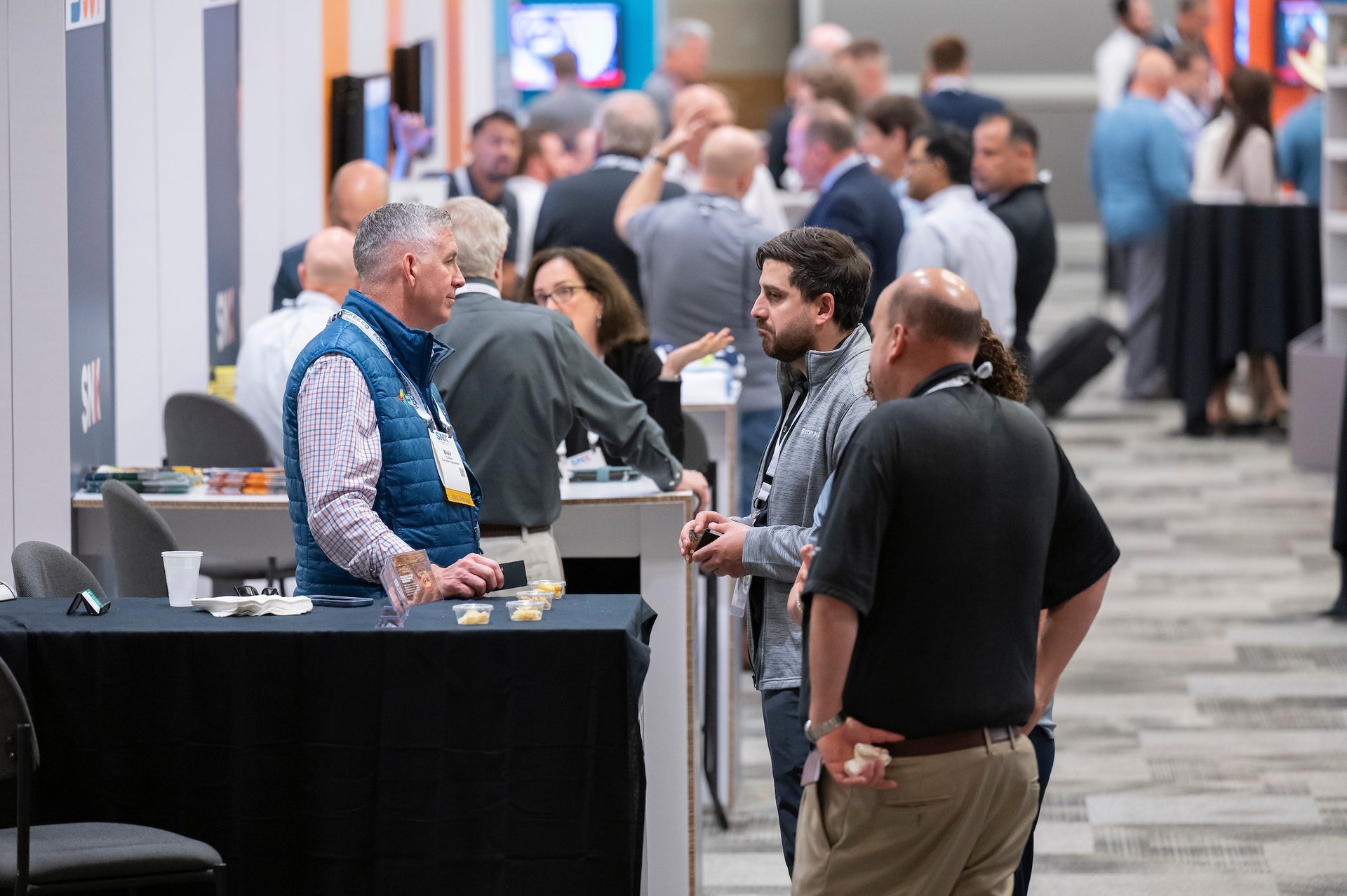 A group of men networking at a conference, with snacks on a table in the foreground.