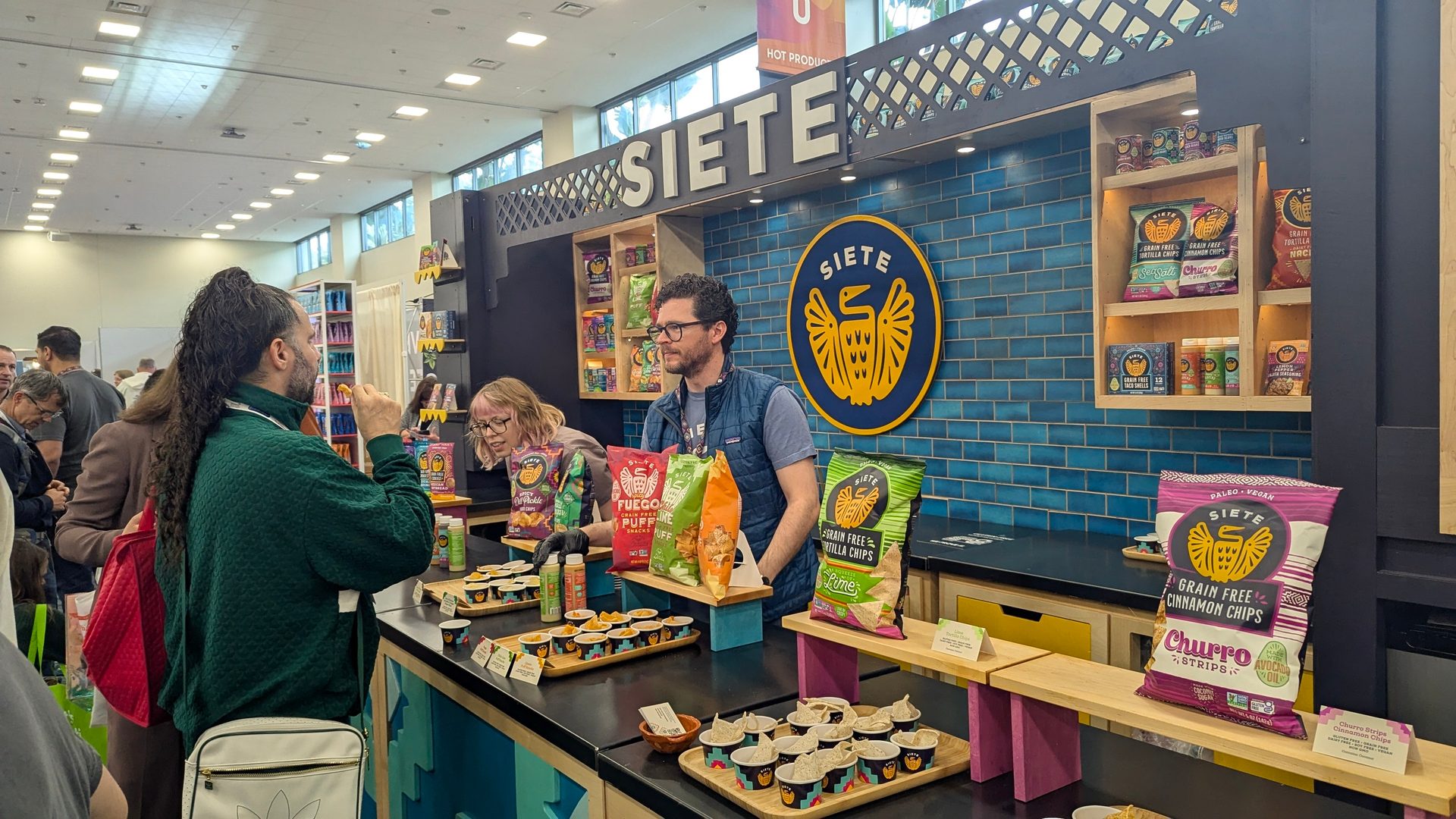 A busy Siete brand booth where people are sampling grain-free chips and snacks.