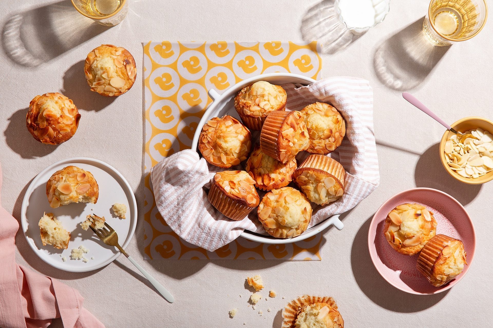 Almond muffins on plates and in a bowl with drinks and napkins, some partially eaten.