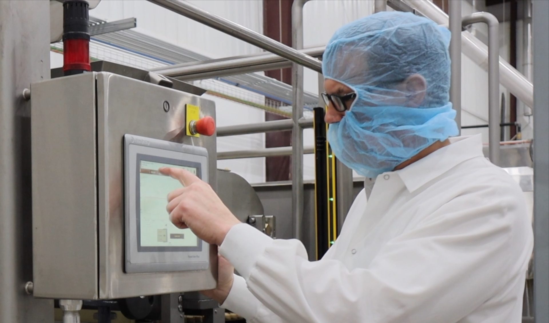 Person in protective gear operating industrial machinery via touchscreen.