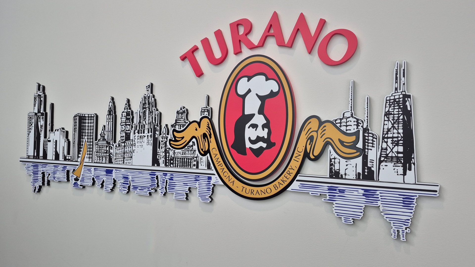 Wall-mounted Turano Bakery sign featuring a red chef logo and black & white Chicago skyline.