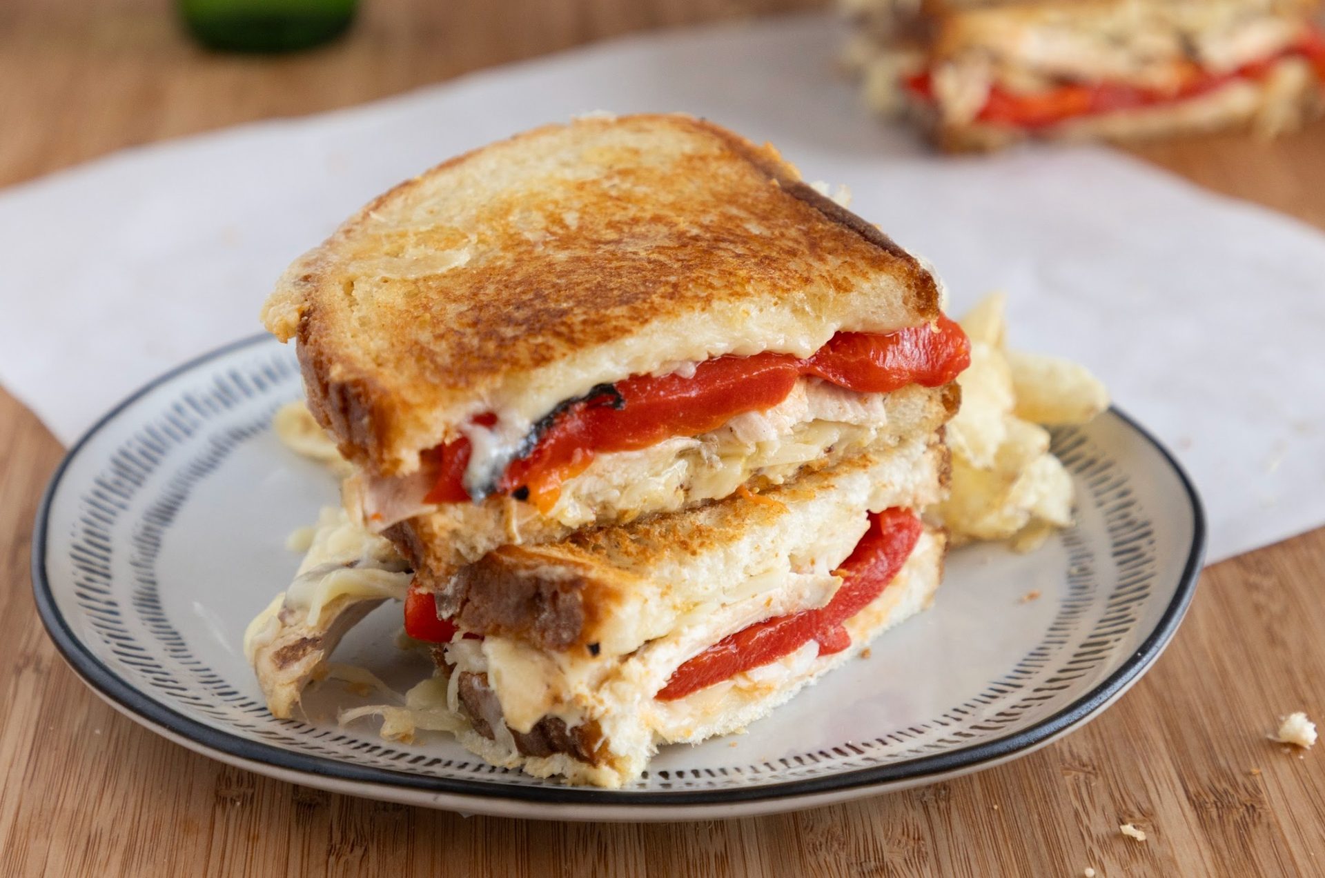Stacked grilled sandwich with red peppers and melted cheese on a plate.
