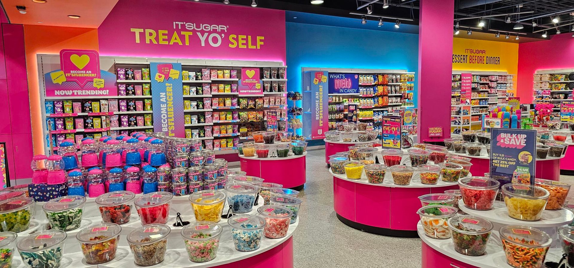 An IT’SUGAR store with pink, green, and yellow walls, and displays of candy.