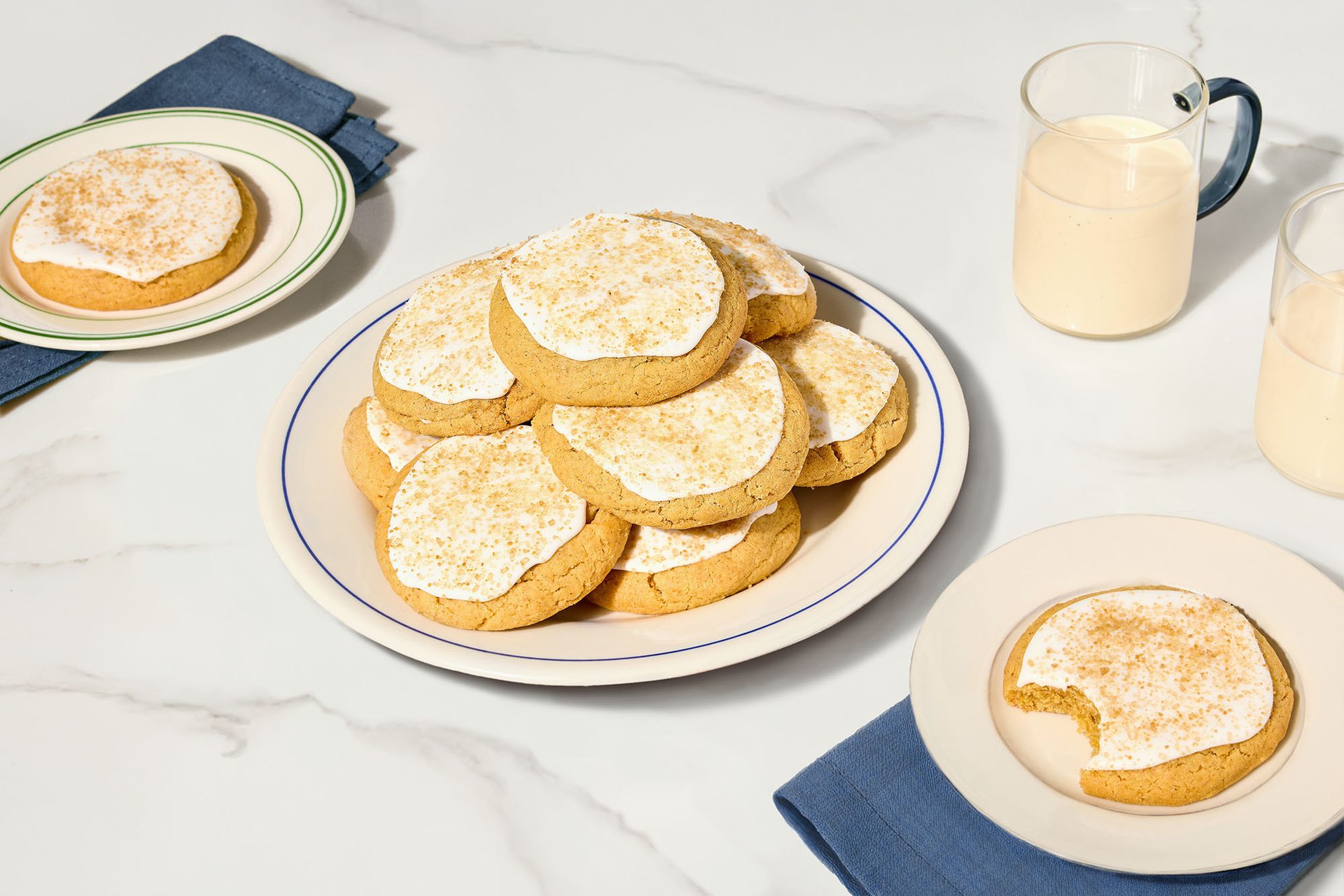 Iced cookies with sprinkles on plates; two glasses of milk on a marble counter.