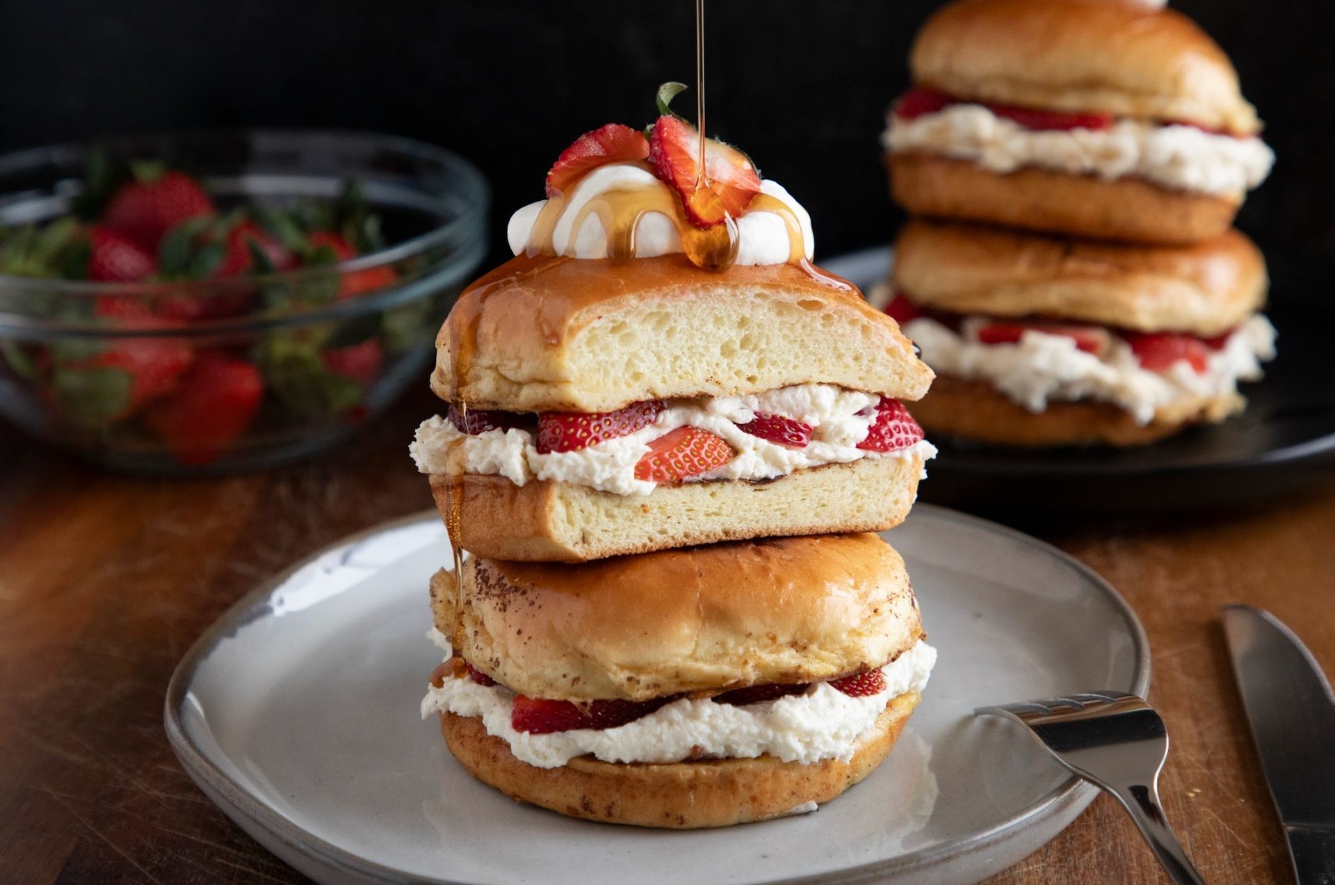 Stacked sweet buns filled with strawberries and whipped cream, drizzled with syrup.
