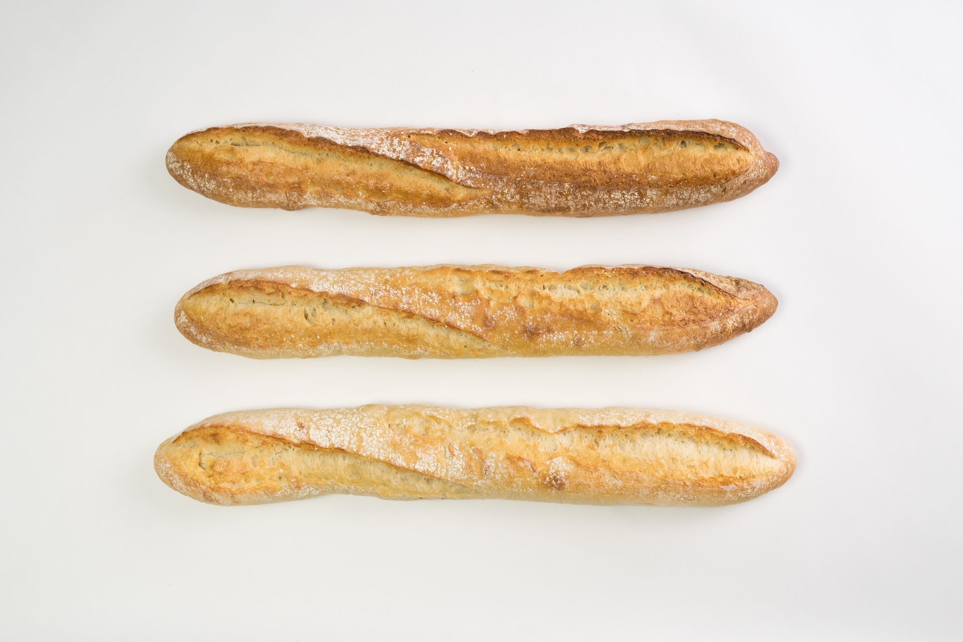 Three freshly baked golden-brown baguettes with crusty tops, arranged horizontally on a white background.