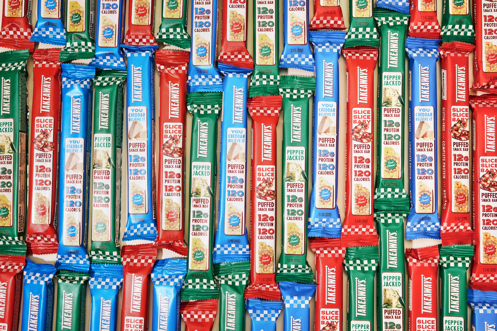 A top-down view of many colorful 'Takeaways' puffed snack bars in red, blue, and green, stacked vertically.