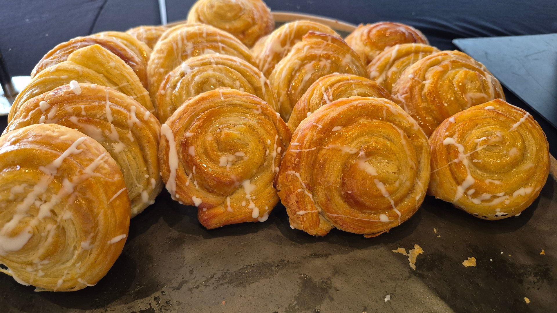Multiple golden pastries with white icing on a dark surface.