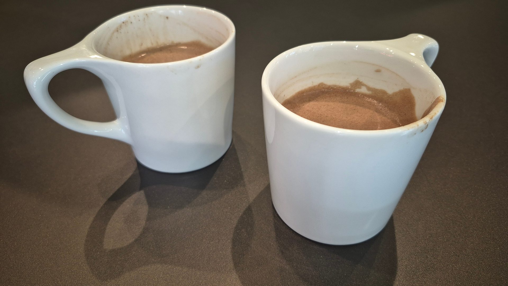 Two white mugs filled with hot chocolate on a dark countertop.