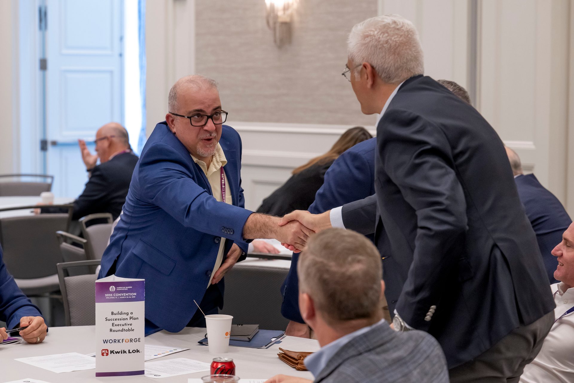 Two men shaking hands at a professional conference or executive roundtable event.