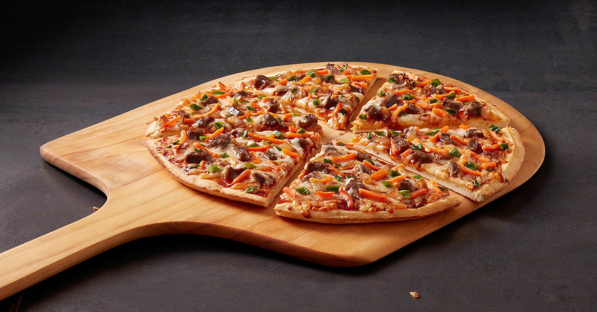 Sliced pizza with beef, carrots, and green peppers on a wooden pizza peel.
