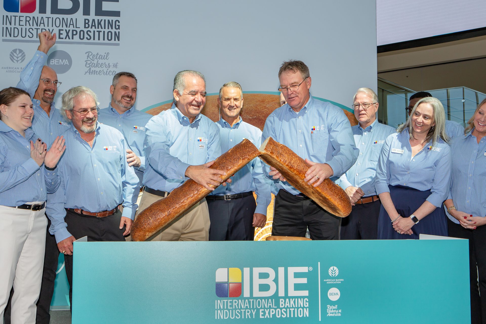 Group of people in blue shirts, two of them holing giant baguette