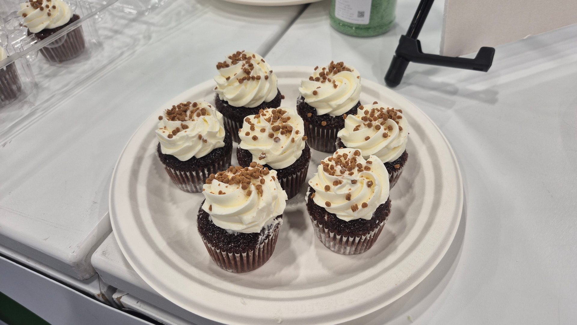 Seven chocolate cupcakes with white frosting and brown sprinkles on a white plate.