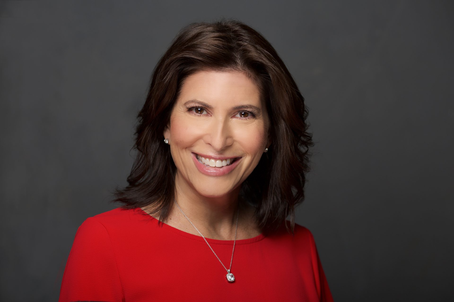 Headshot of a smiling woman with brown hair wearing a red top and a necklace.