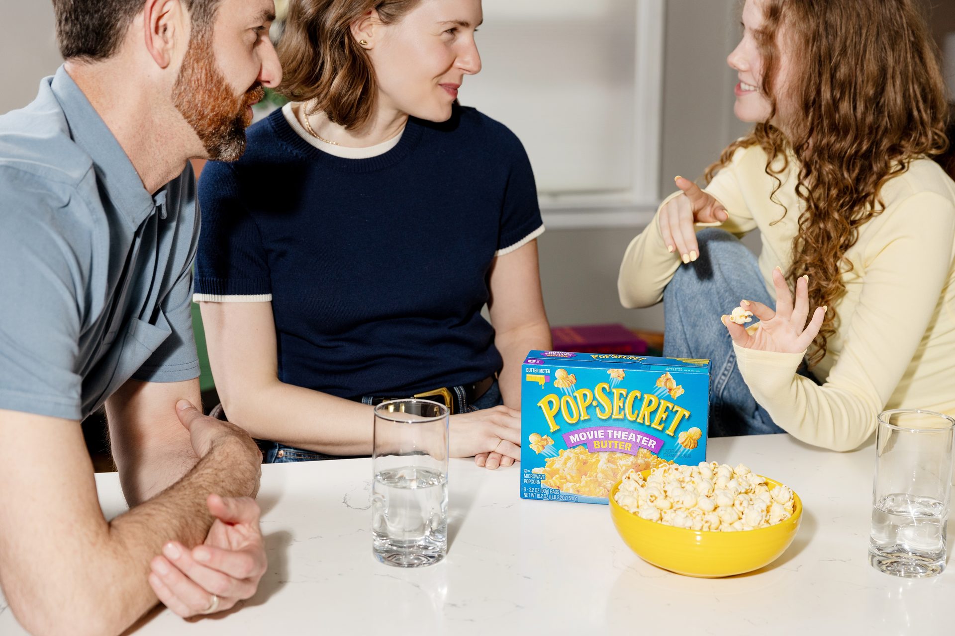 Three people gathered around a table, enjoying popcorn and water, with a Pop Secret box.