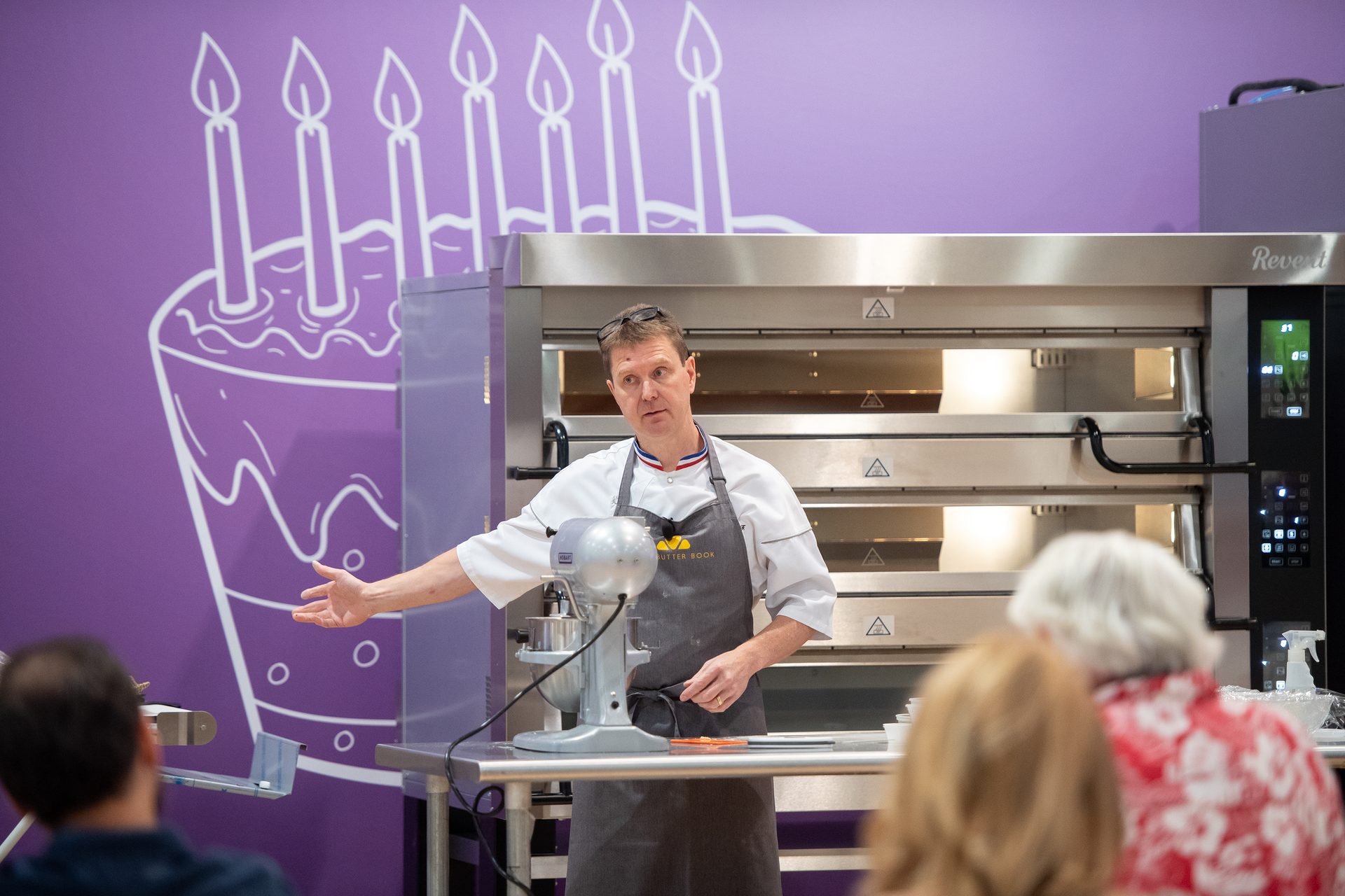 Man in apron between table with mixer and baking ovens