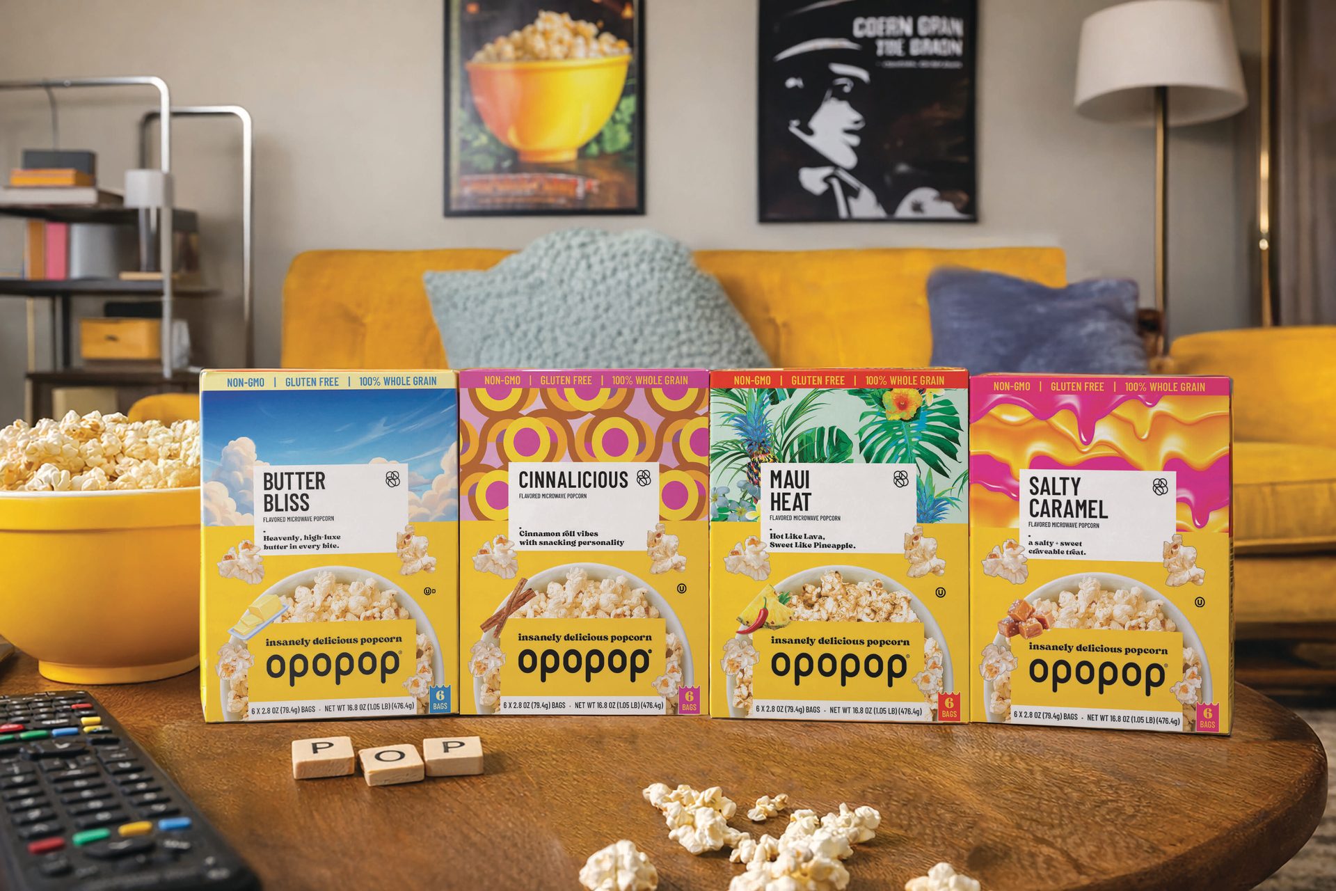 Four Opopop microwave popcorn boxes and a bowl of popcorn on a coffee table with a remote.