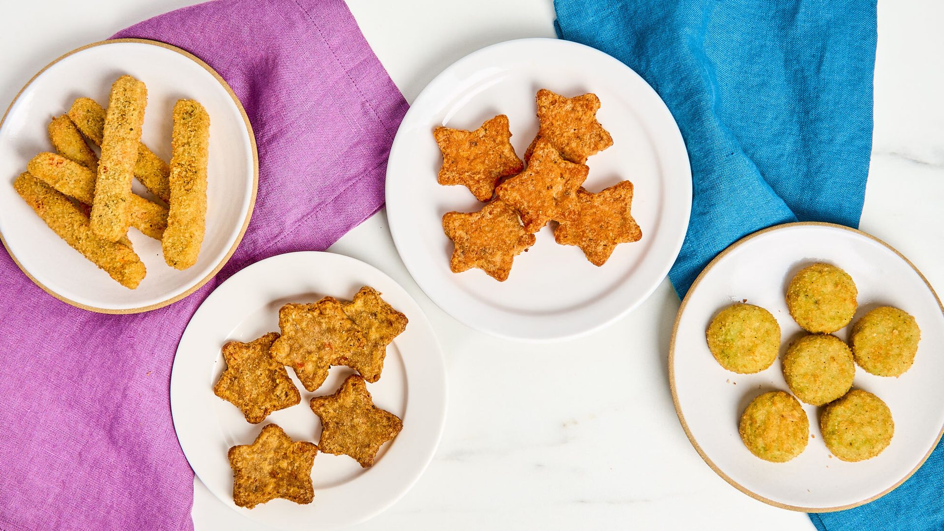 Assorted fried snacks on four plates: golden sticks, star-shaped, and green rounds.