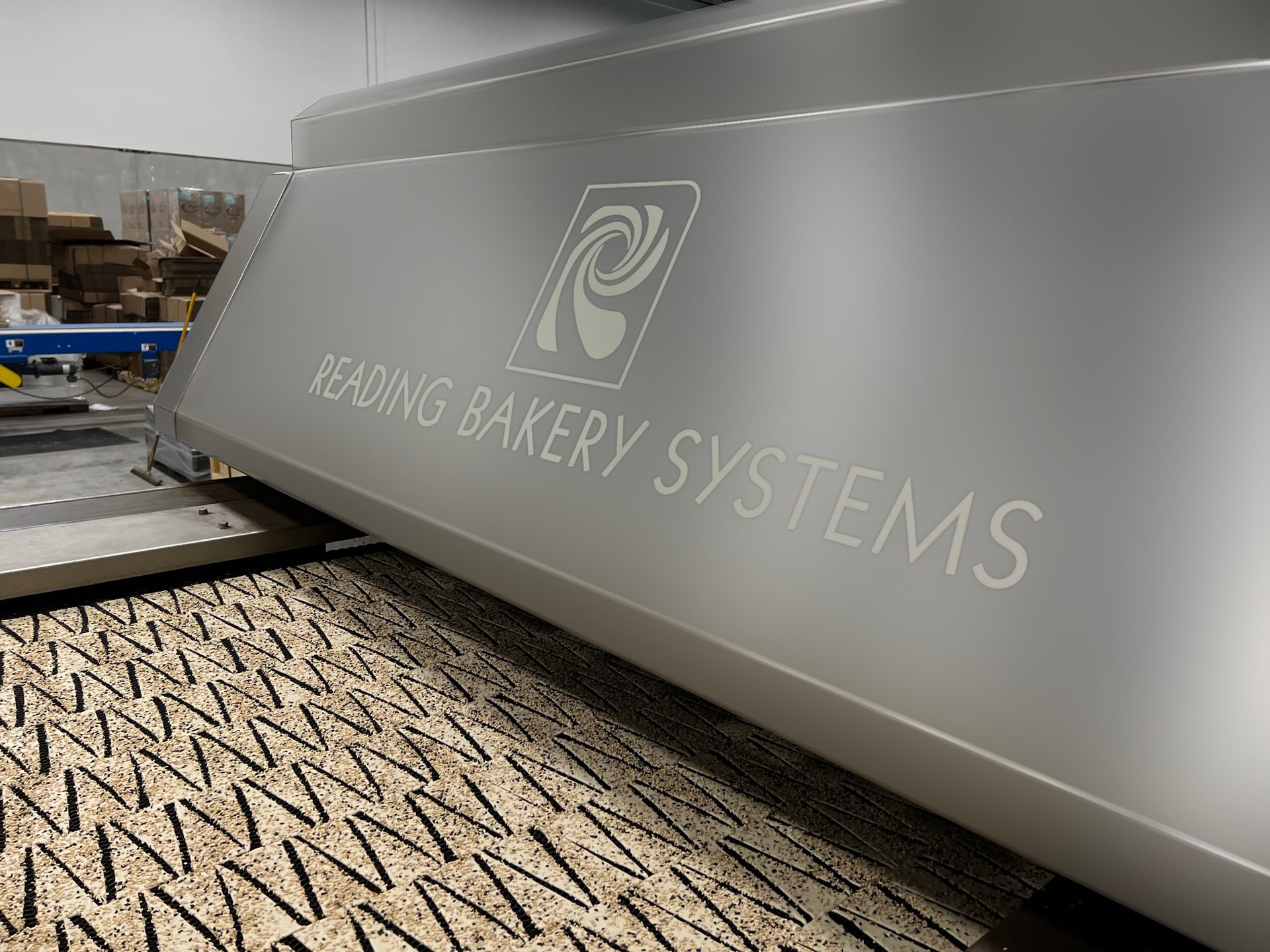 Reading Bakery Systems machine with logo, processing patterned food items on a conveyor belt.