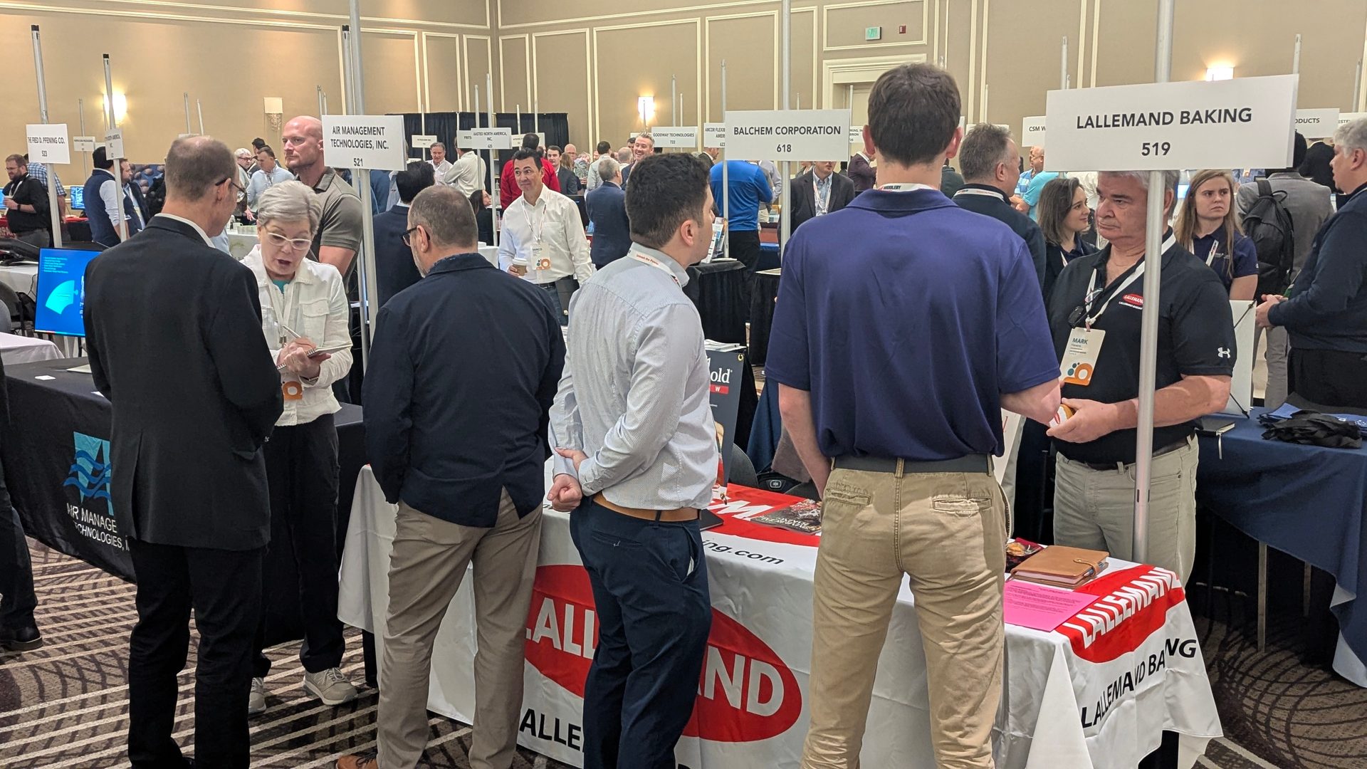 A busy trade show with many people networking around company booths.