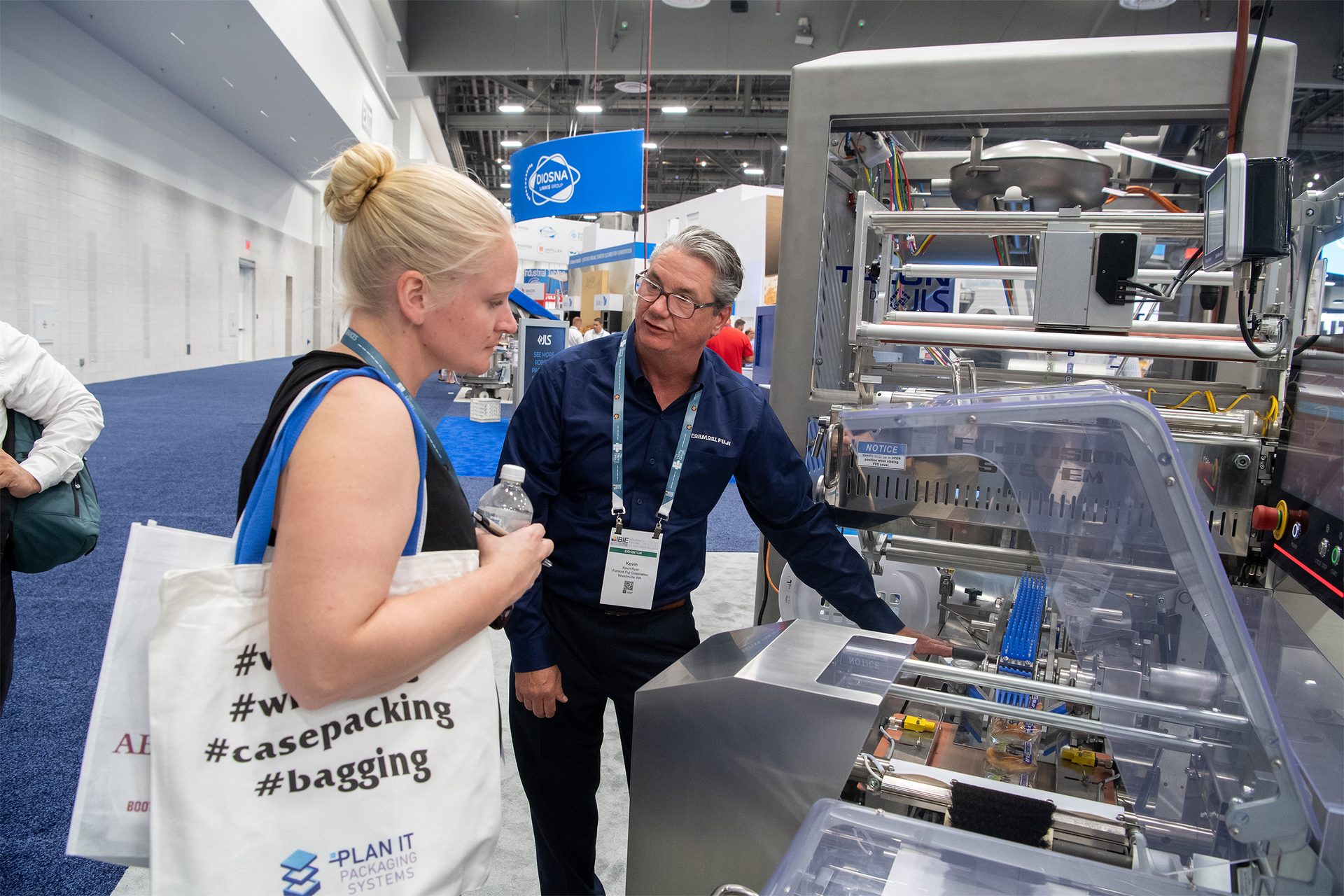 Woman holding tote bag talking to man, examining baking equipment