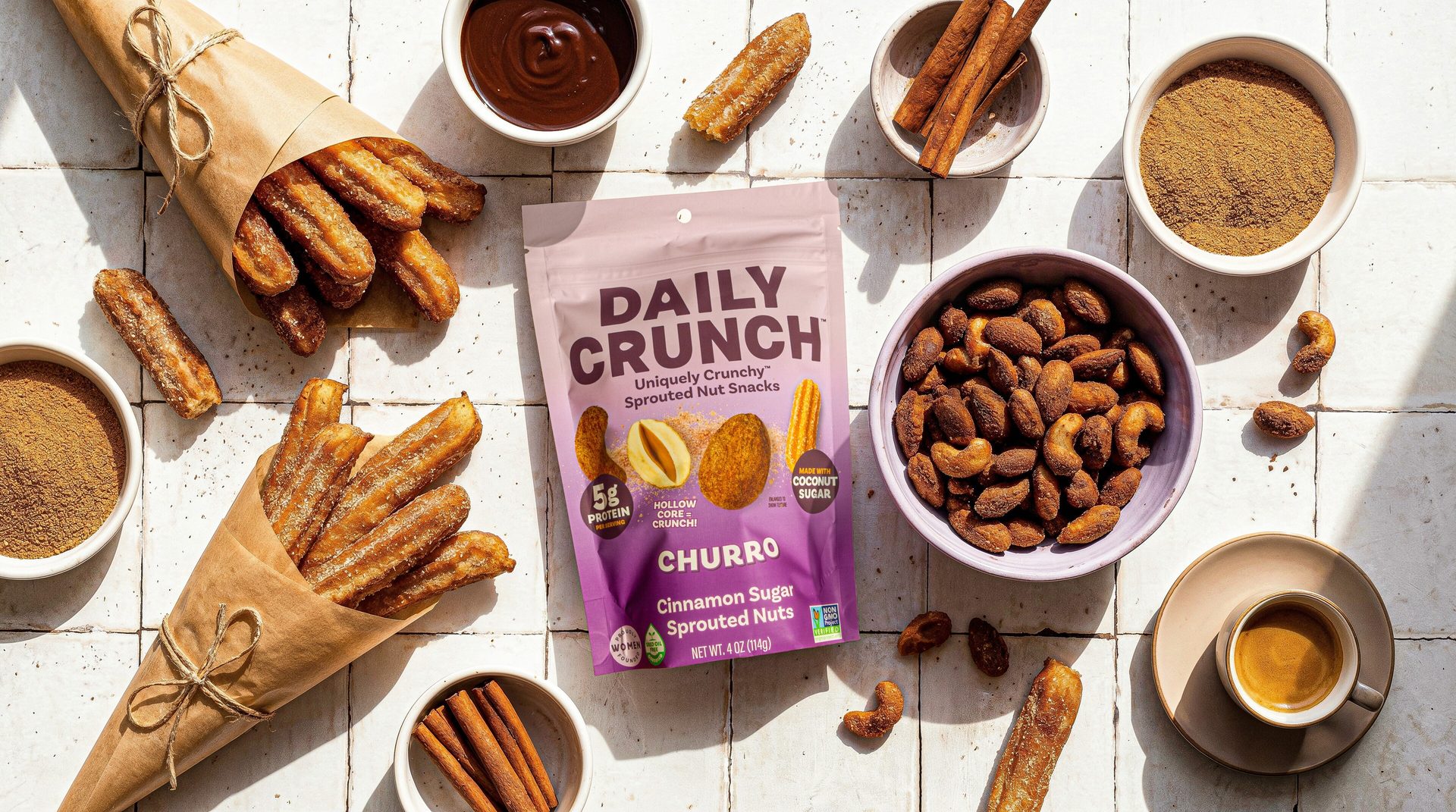 Daily Crunch Churro Cinnamon Sugar Sprouted Nuts snack bag surrounded by churros, chocolate, cinnamon, and nuts.
