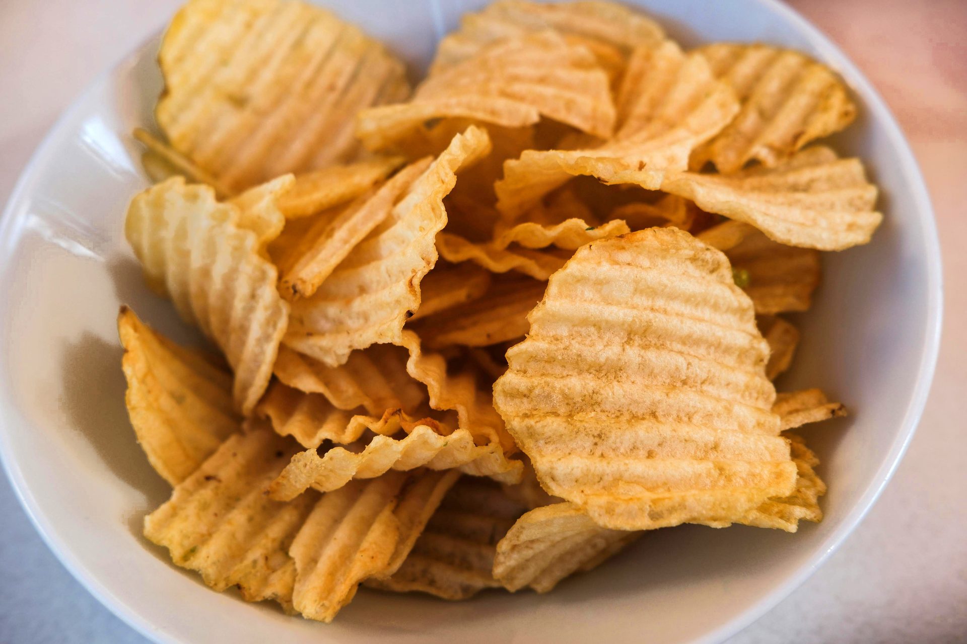 A white bowl filled with golden, crinkle-cut potato chips, presenting a savory, crunchy snack.